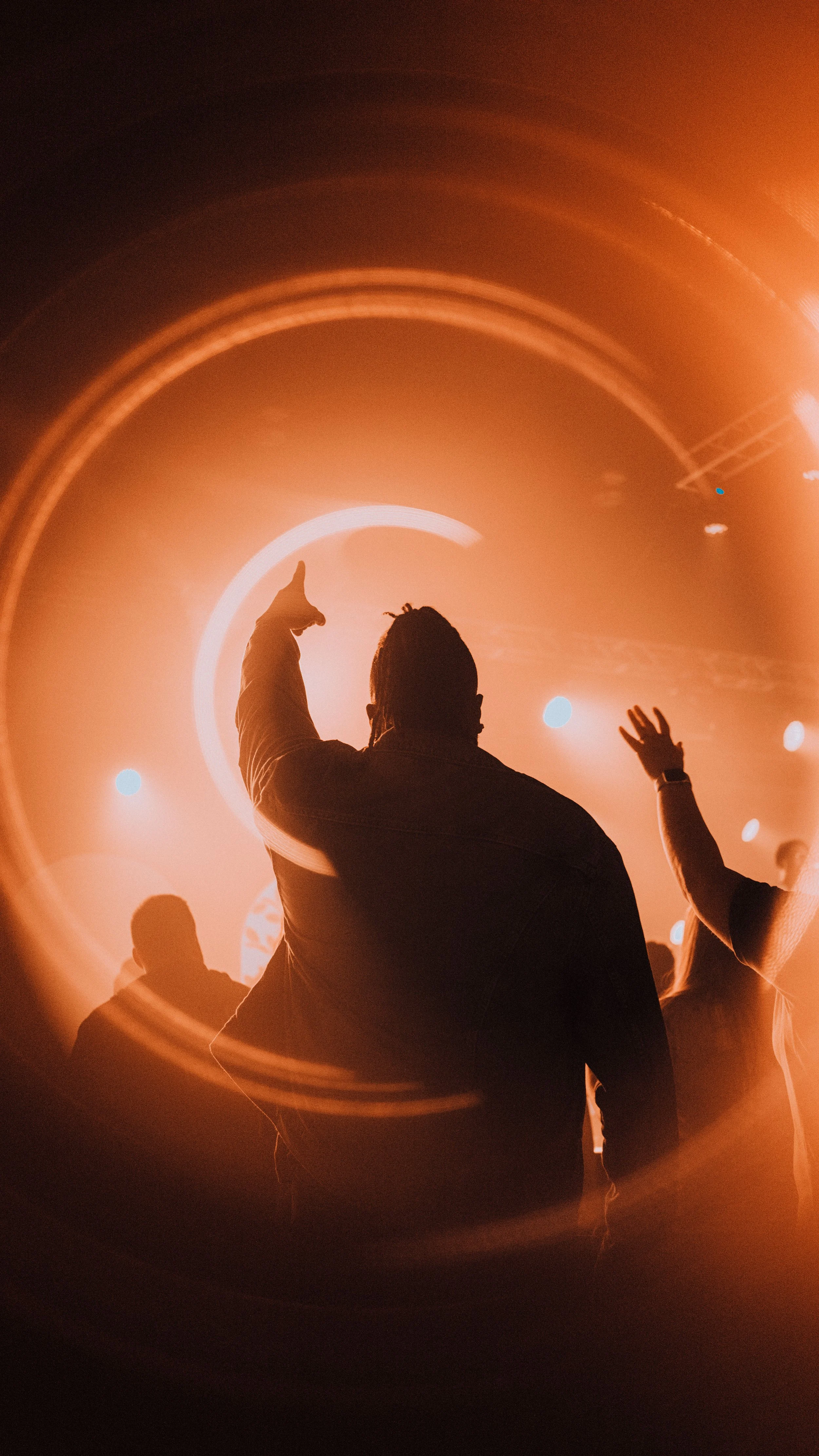Silhouettes of people enjoying a live concert or music event, with stage lights and circular lighting effects creating a vibrant atmosphere.