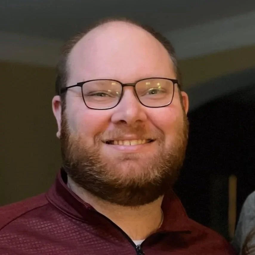 A man with glasses, beard, and short hair smiling at the camera.