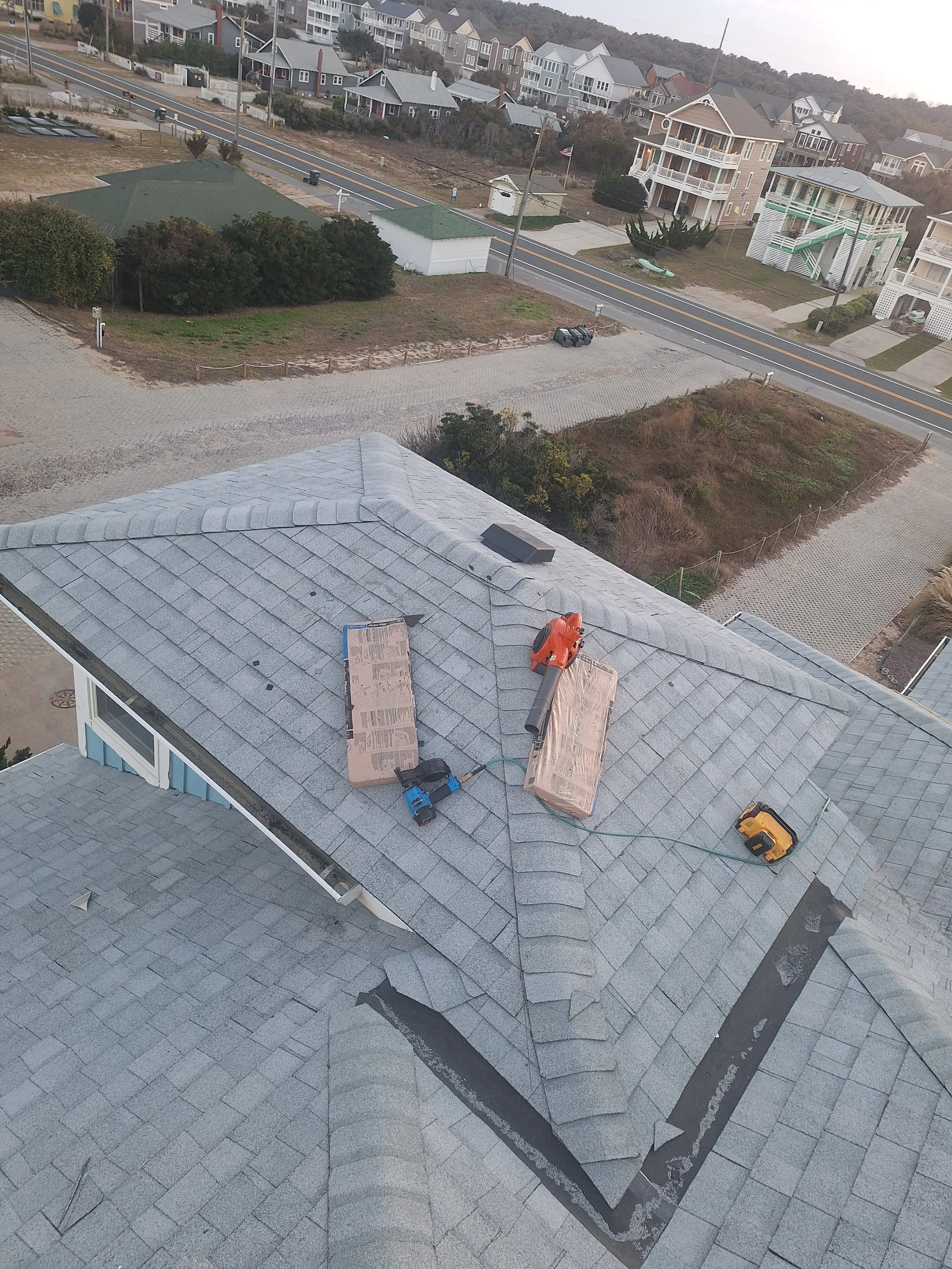 View from above of a residential roof under maintenance with tools, including a power drill, a leaf blower, and a yellow measuring tape.