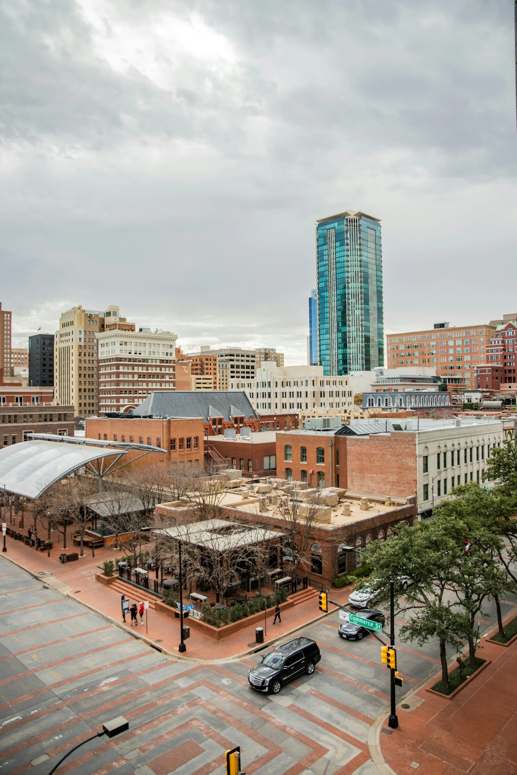 Fort Worth cityscape with a mix of modern and historic buildings, overcast sky, street with cars and pedestrians at an intersection.