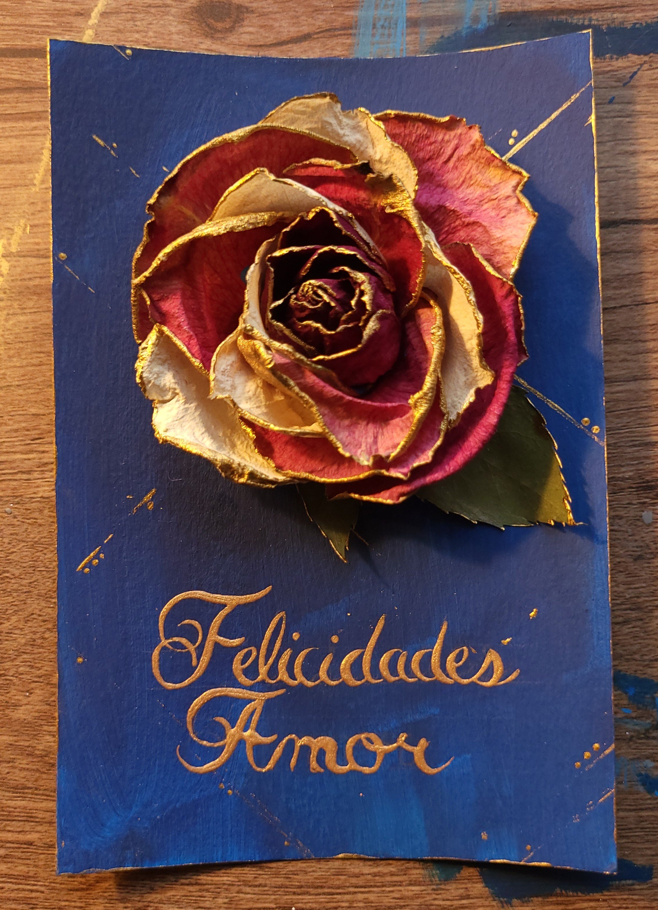 acrylic painting with a rose-like flower in the center. Text reads "Felicidades Amor"