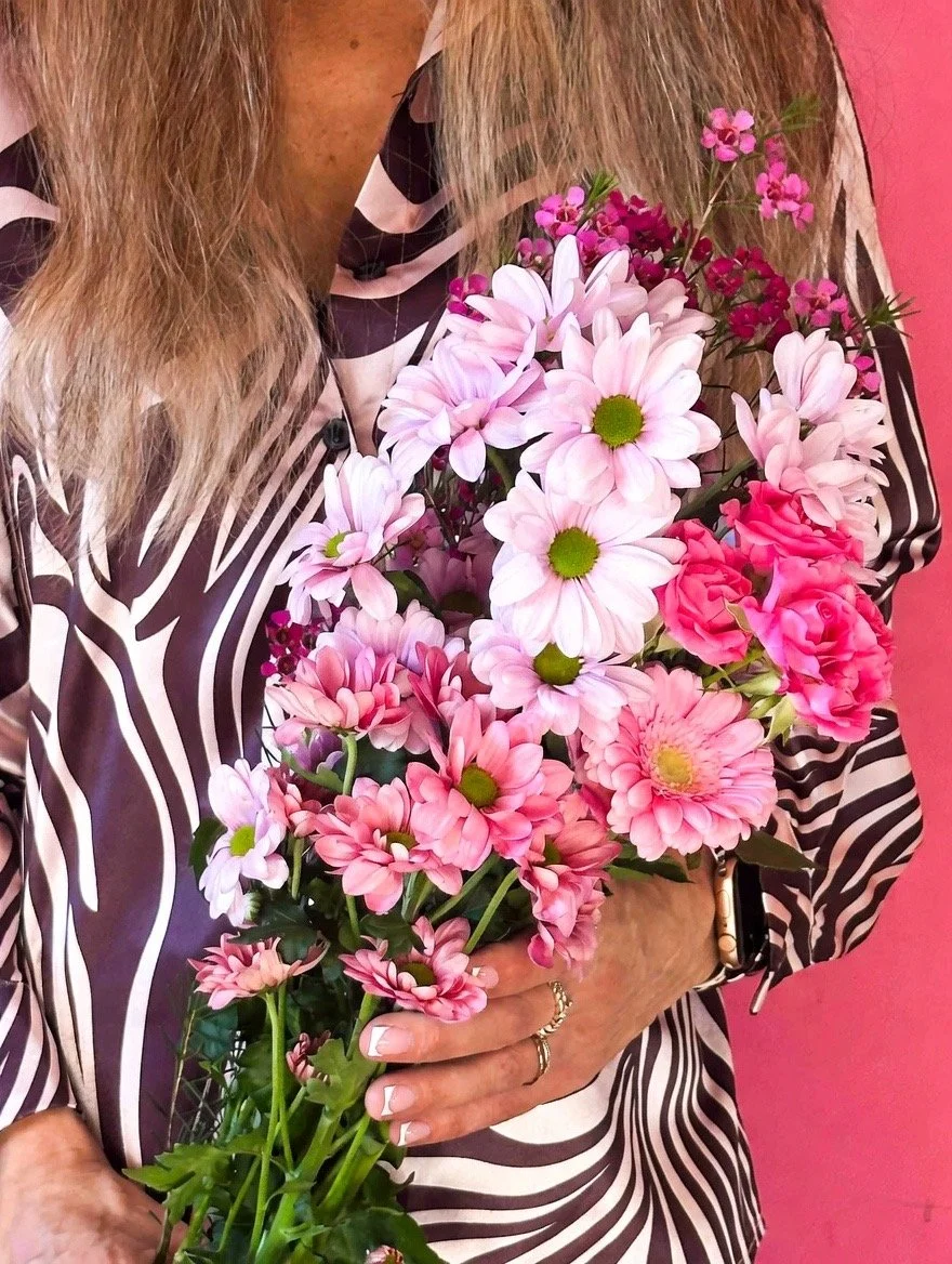 Person holding a bouquet of pink and white flowers in front of a pink background.