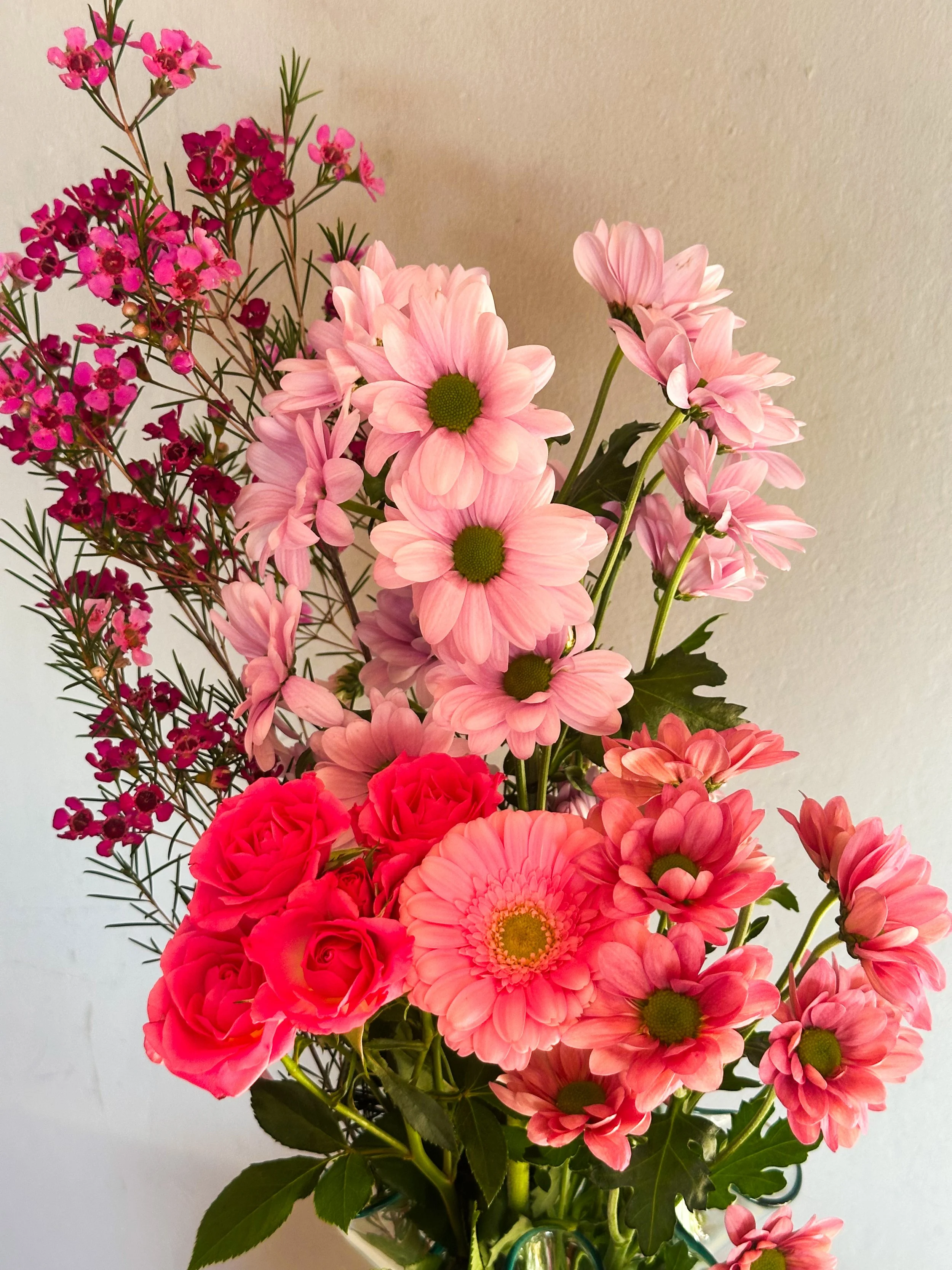 A bouquet of pink and red flowers, including daisies, roses, and other blossoms, arranged in a vase.