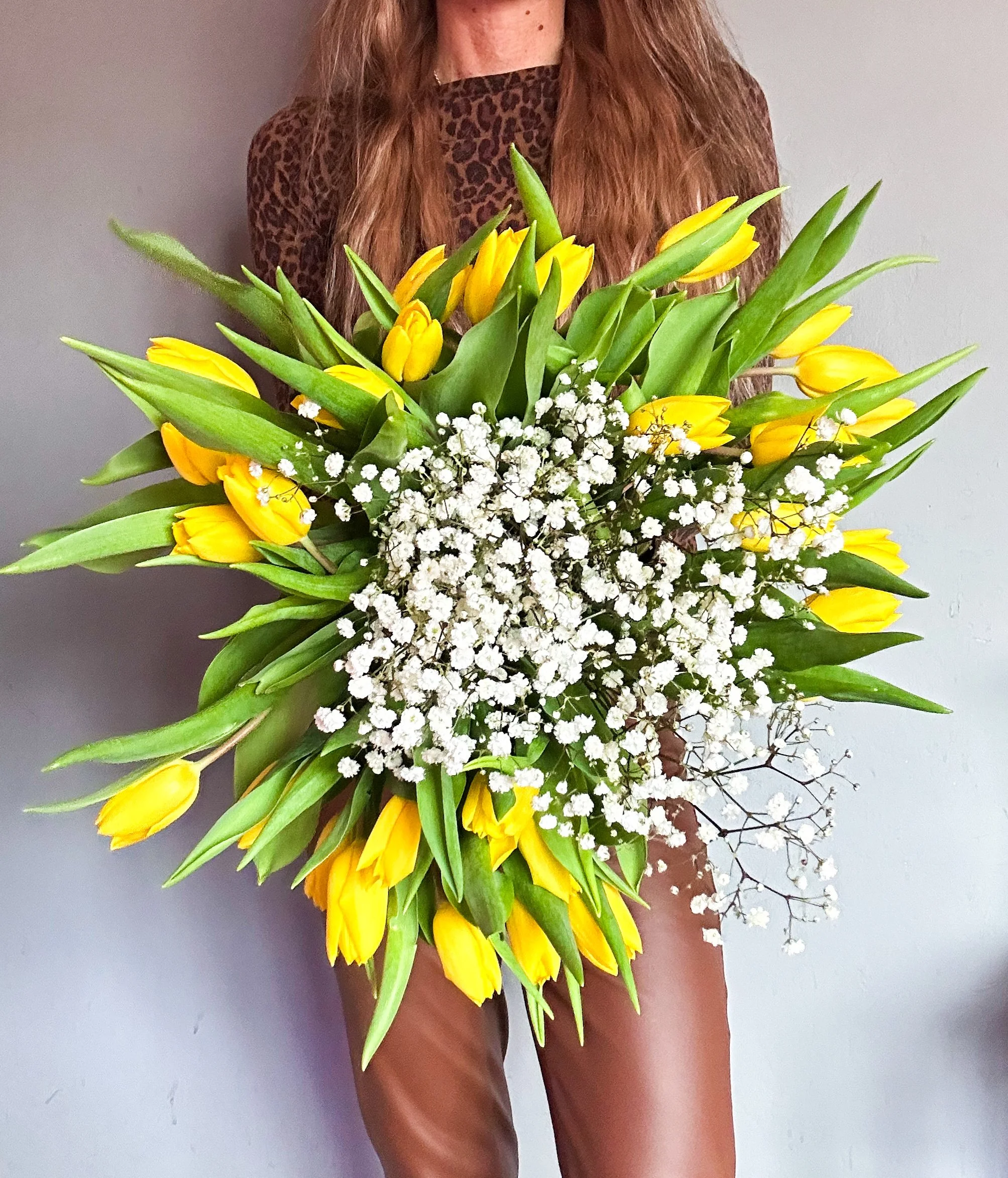 Person holding a large bouquet of yellow tulips and white baby's breath flowers.
