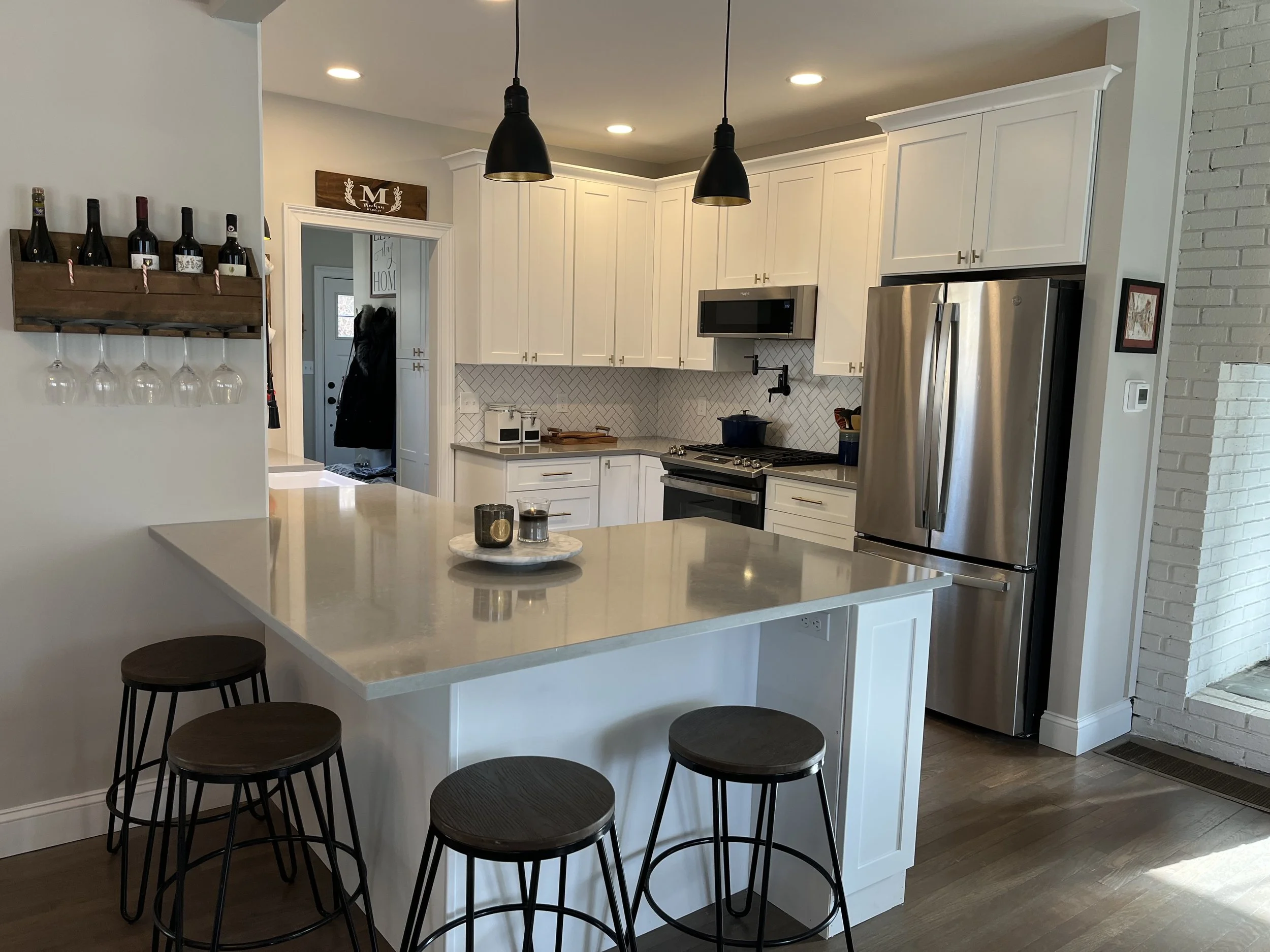 Modern kitchen with white cabinets, a marble island, stainless steel refrigerator, pendant lights, and barstools.