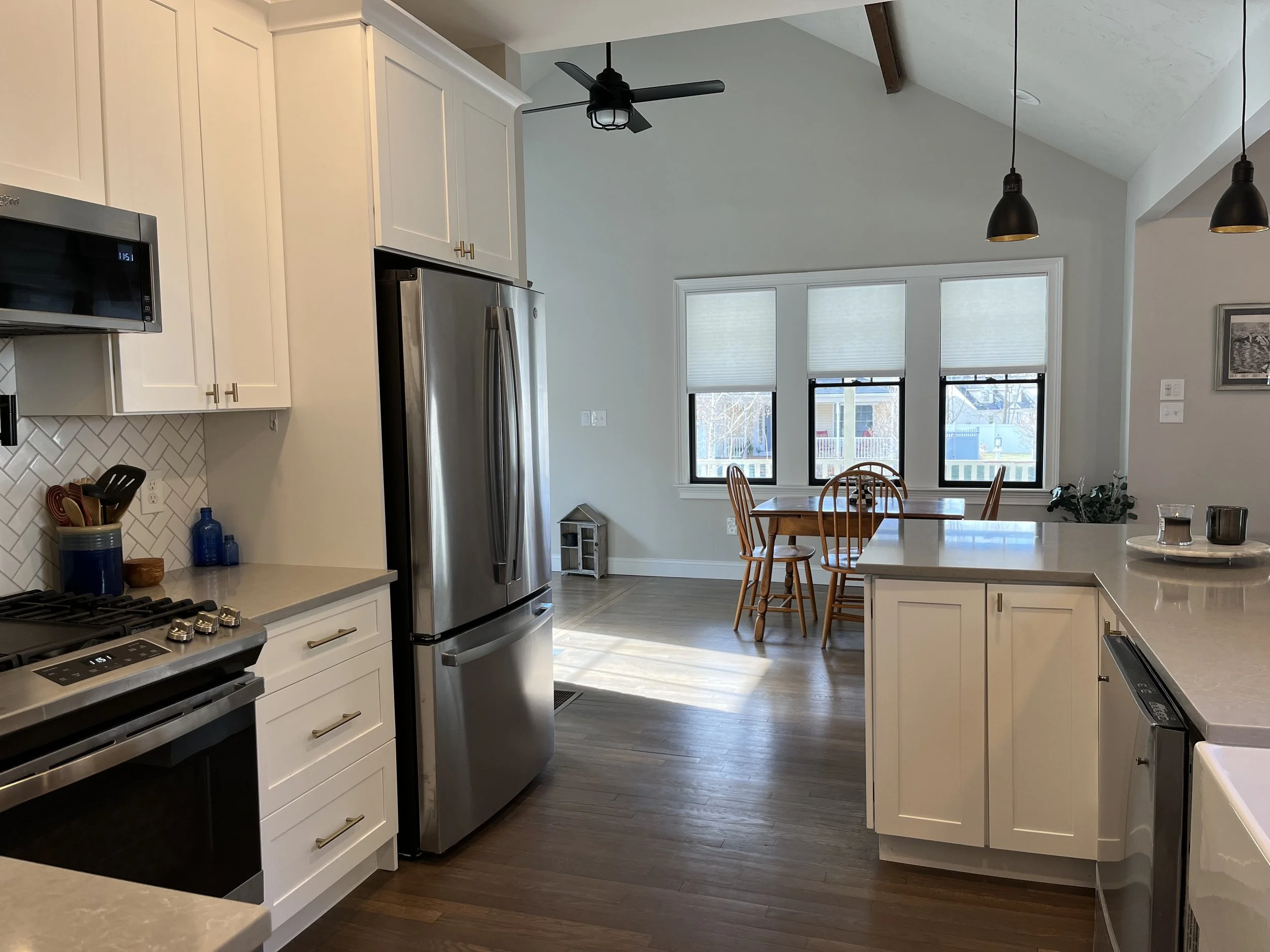 Modern kitchen with white cabinets, stainless steel appliances, and a dining area with wooden table and chairs near three windows.