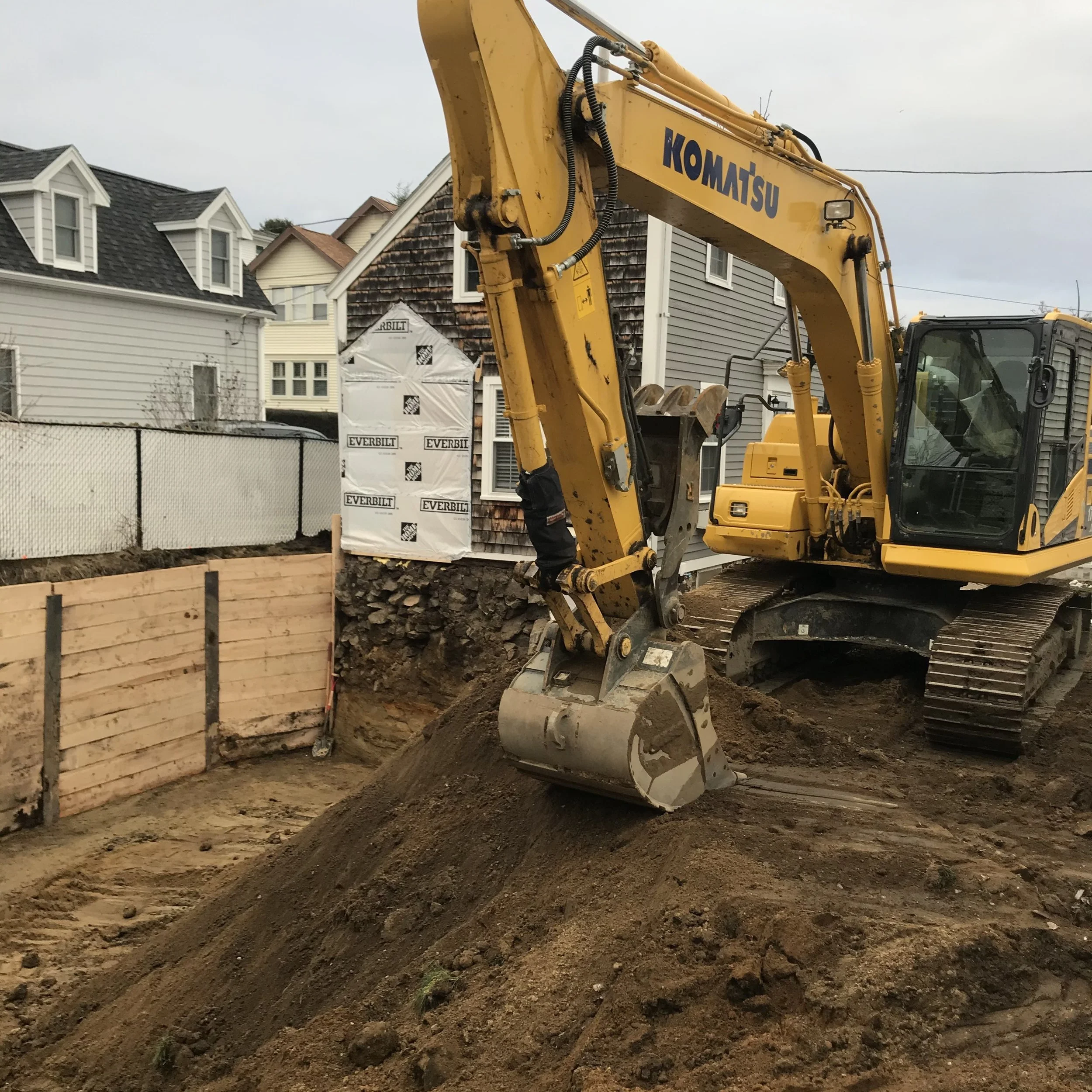 A yellow Komatsu excavator moving dirt on a construction site with residential houses in the background.