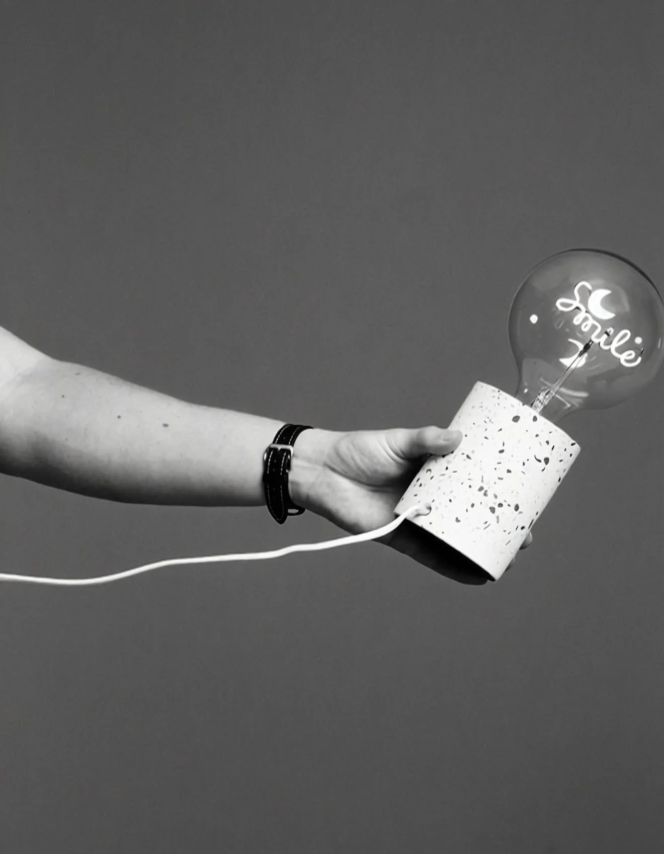 A person holding a textured lamp resembling a speaker with a lightbulb inside that has the word 'smile' written on it, against a plain background.