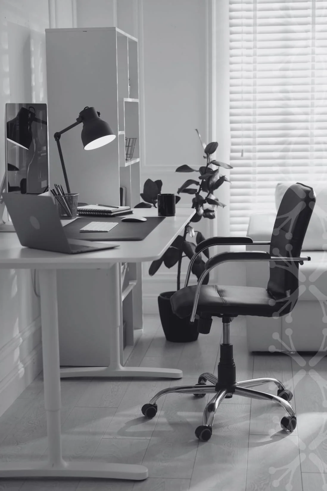A modern home office with a white desk, black office chair, desktop computer, laptop, desk lamp, and various office supplies, with a window covered by blinds in the background.