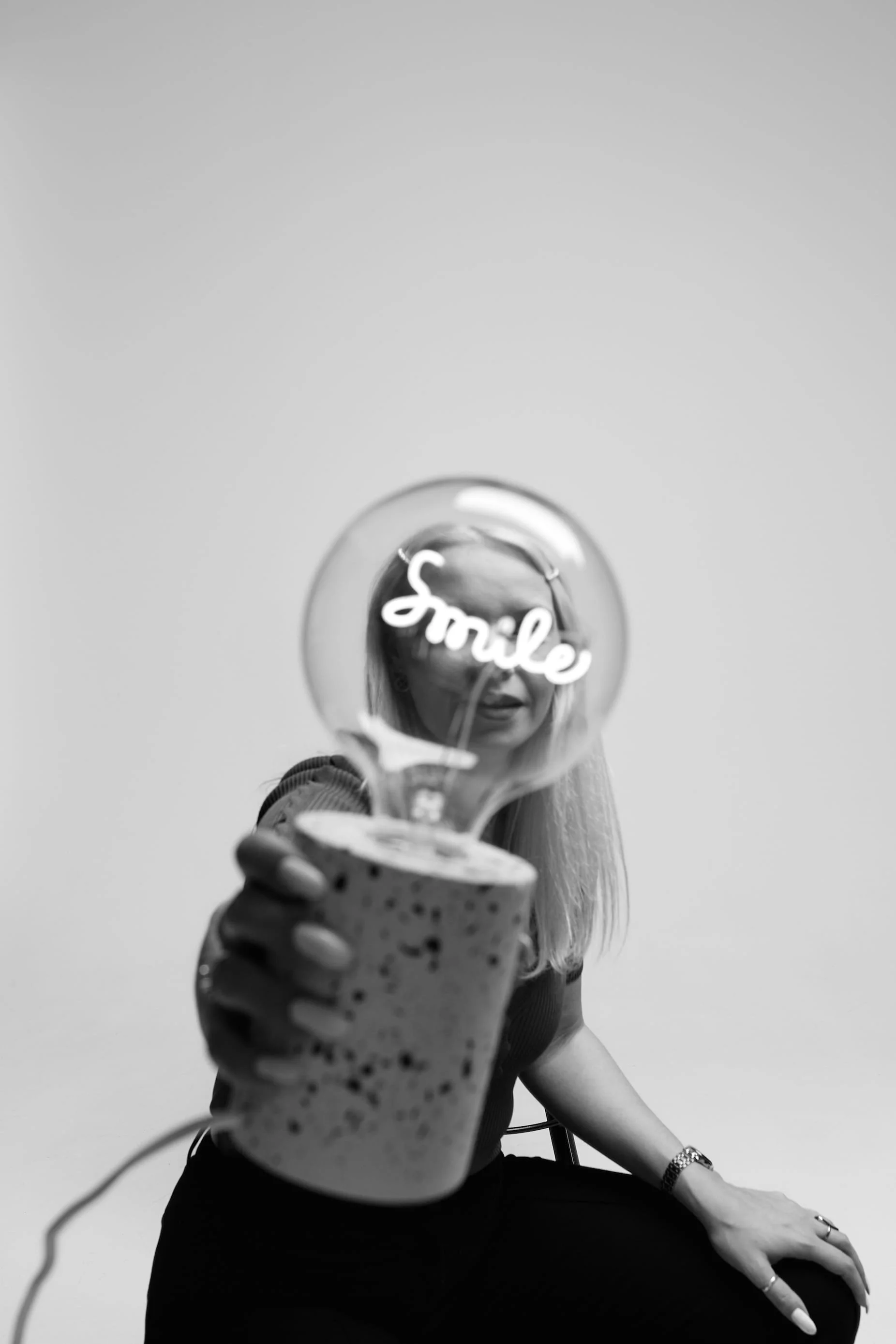 A woman, Larissa, founder of GlassFrog sitting and holding a large bulb with the word 'Smile' written on it.