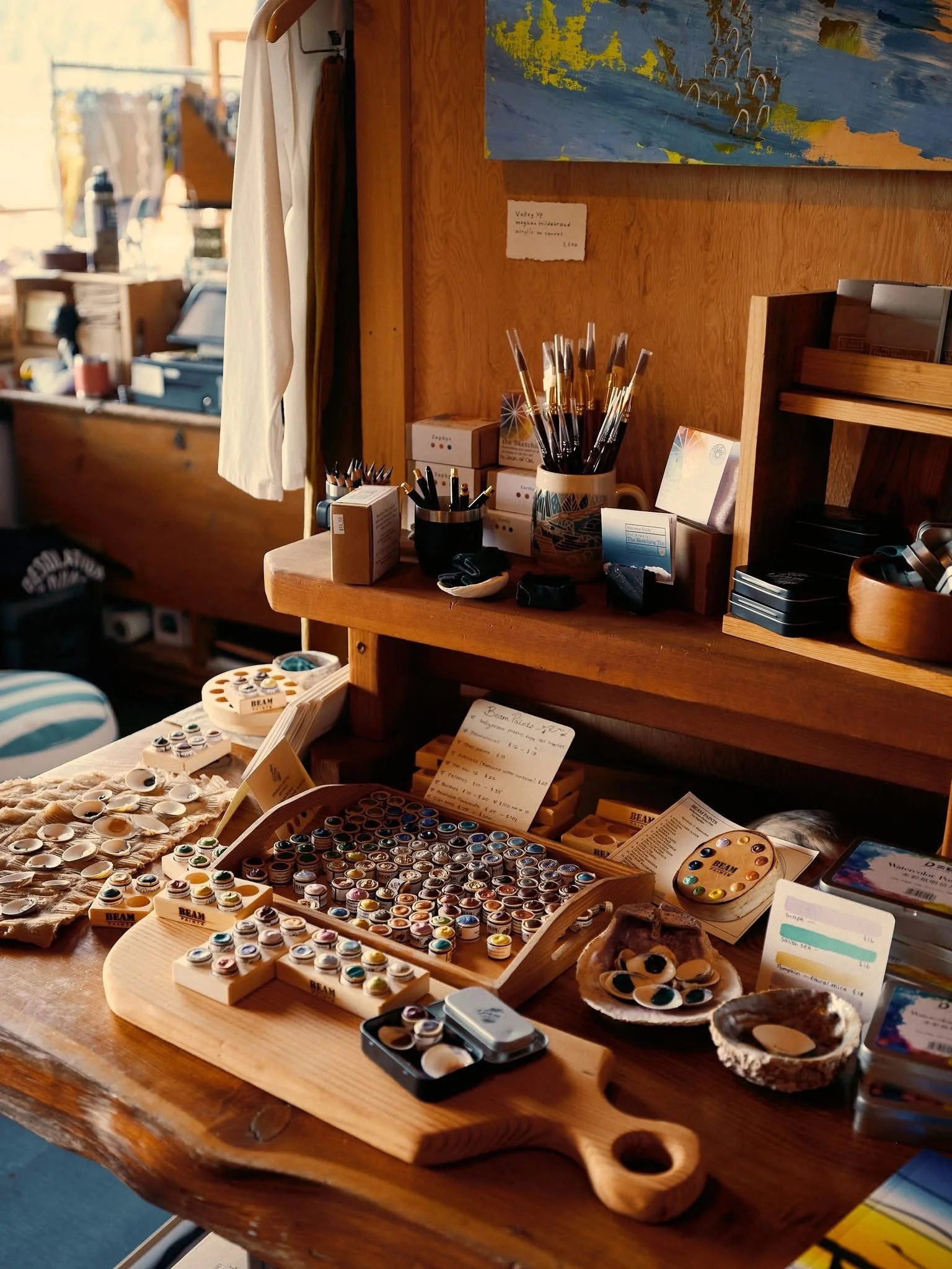 Art supplies and shells on a wooden table at a craft fair or market stall.