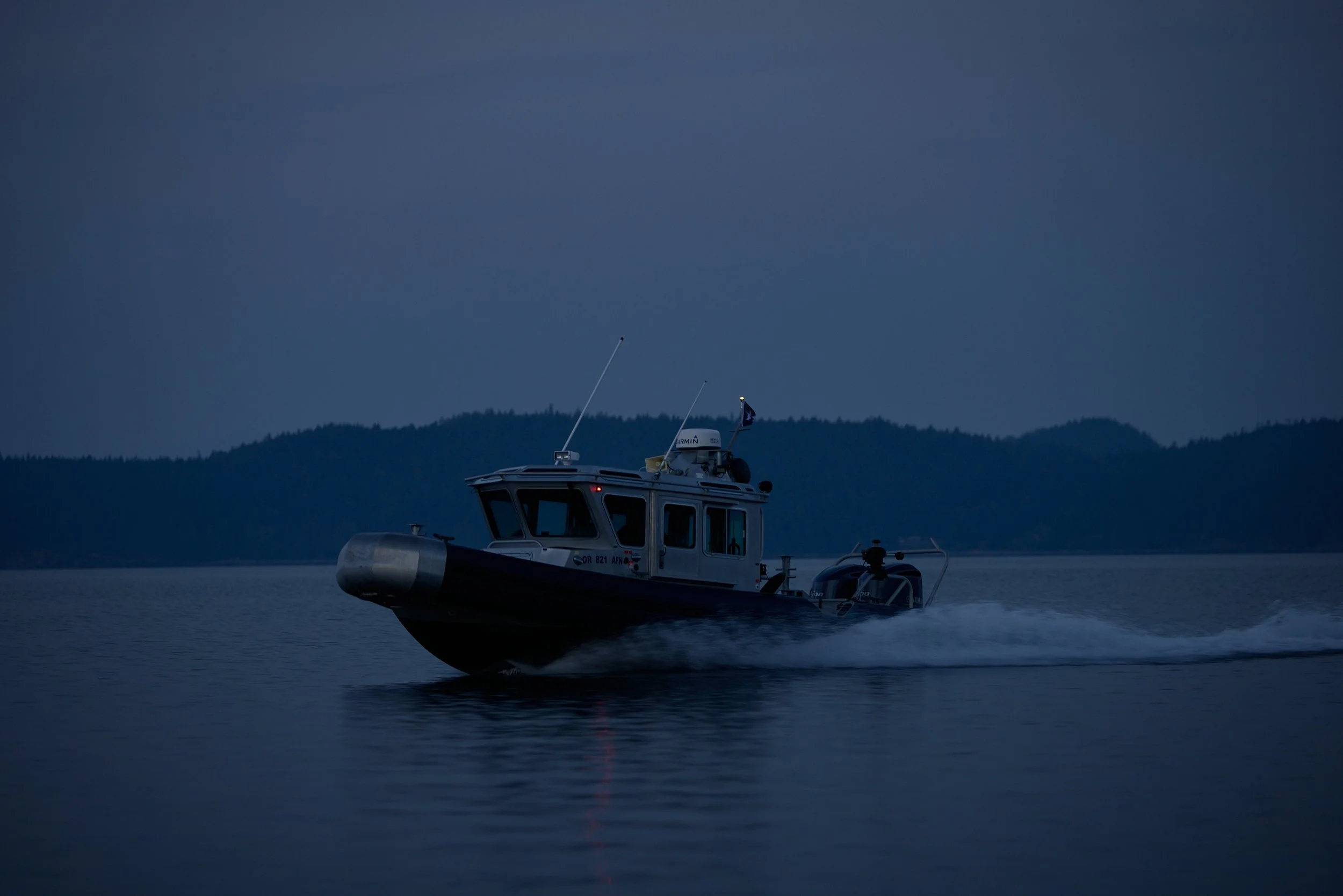 A boat on a body of water during dusk with the silhouette of mountains in the background.