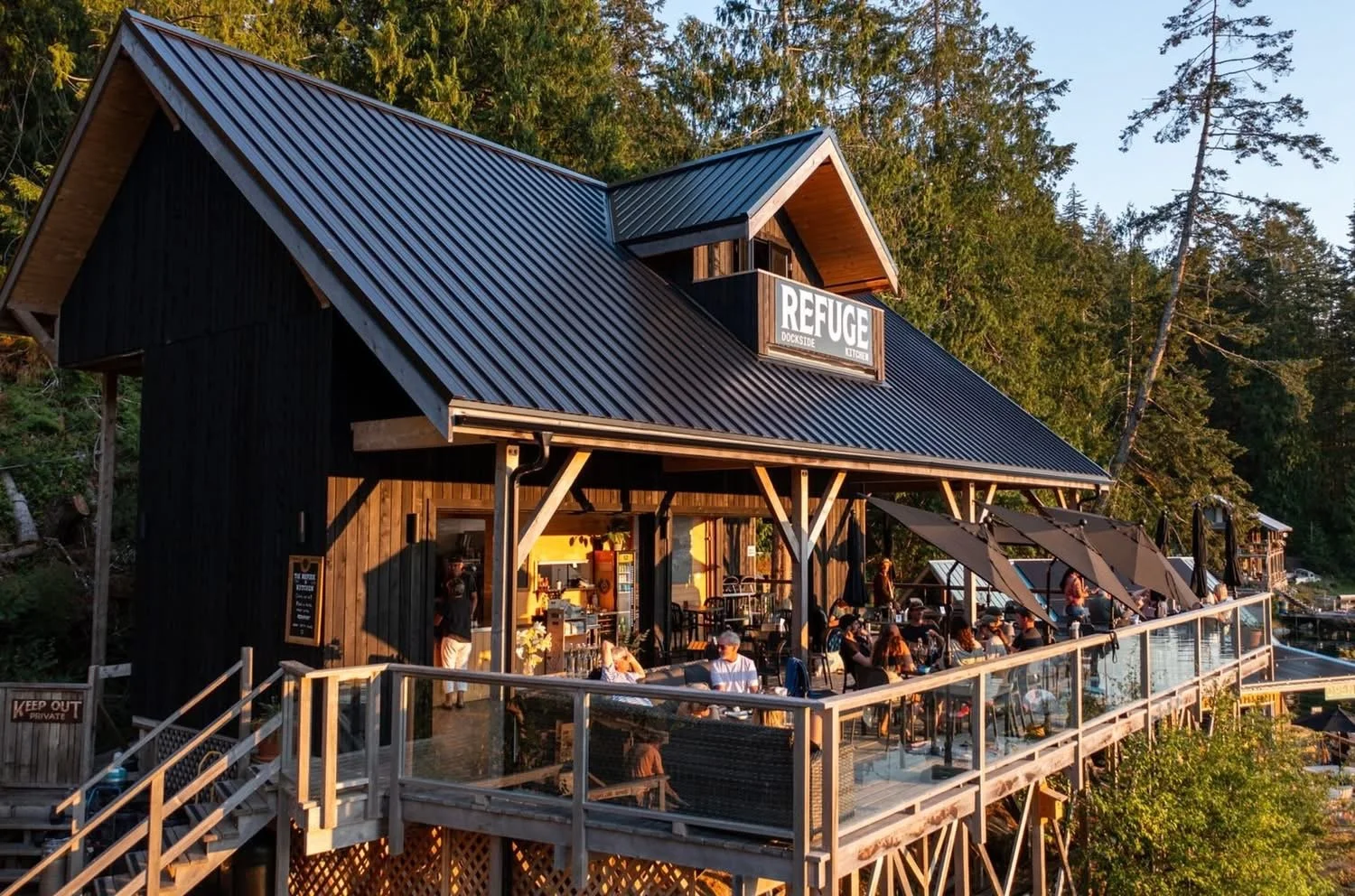 A two-story wooden building with a balcony and a black metal roof, labeled 'Refuge Dockside.