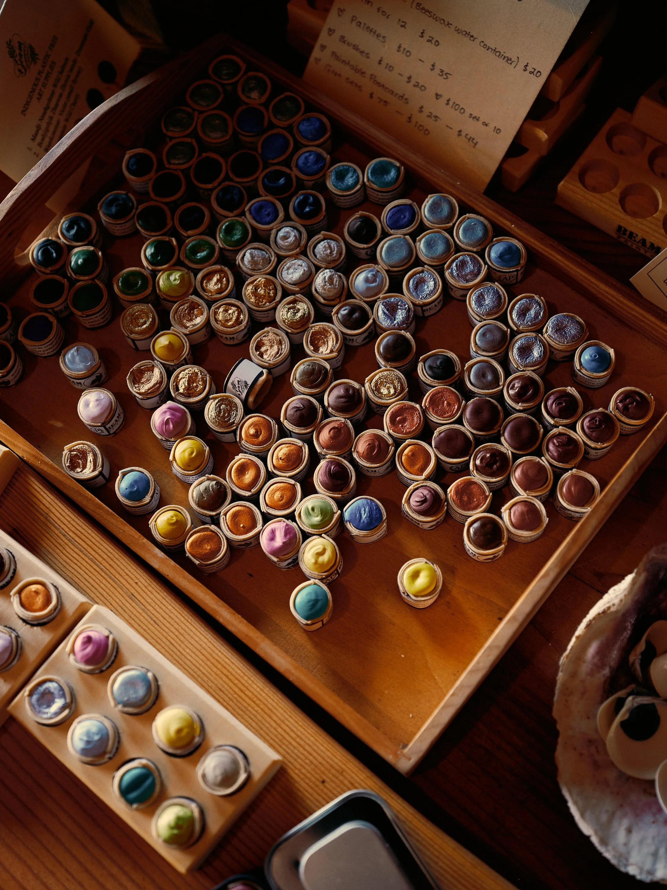A display of small pots of watercolor paints in various colors arranged in wooden trays.