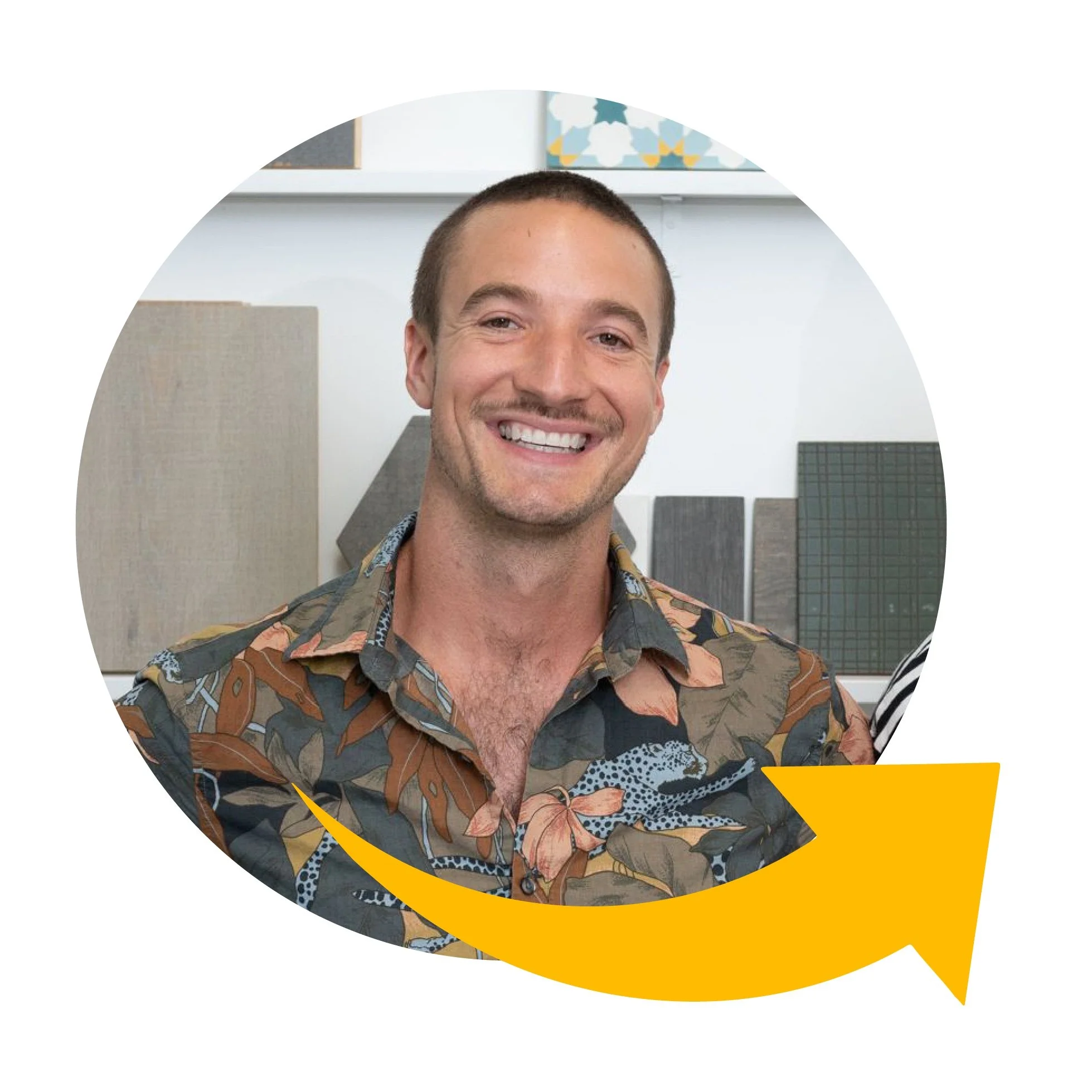 Smiling man with short brown hair and a patterned button-up shirt, standing in front of a white wall with framed artwork and sample tiles.