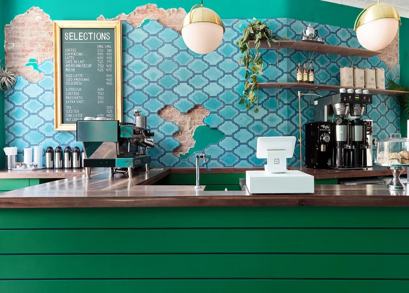 Interior of a coffee shop with a counter, espresso machine, menu board, and decorative wall with colorful tiles.