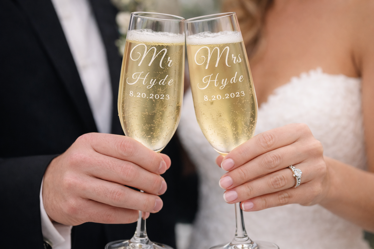 Close-up of a bride and groom holding champagne flutes engraved with 'Mr Mrs Hyde 8.20.2023' at their wedding celebration.