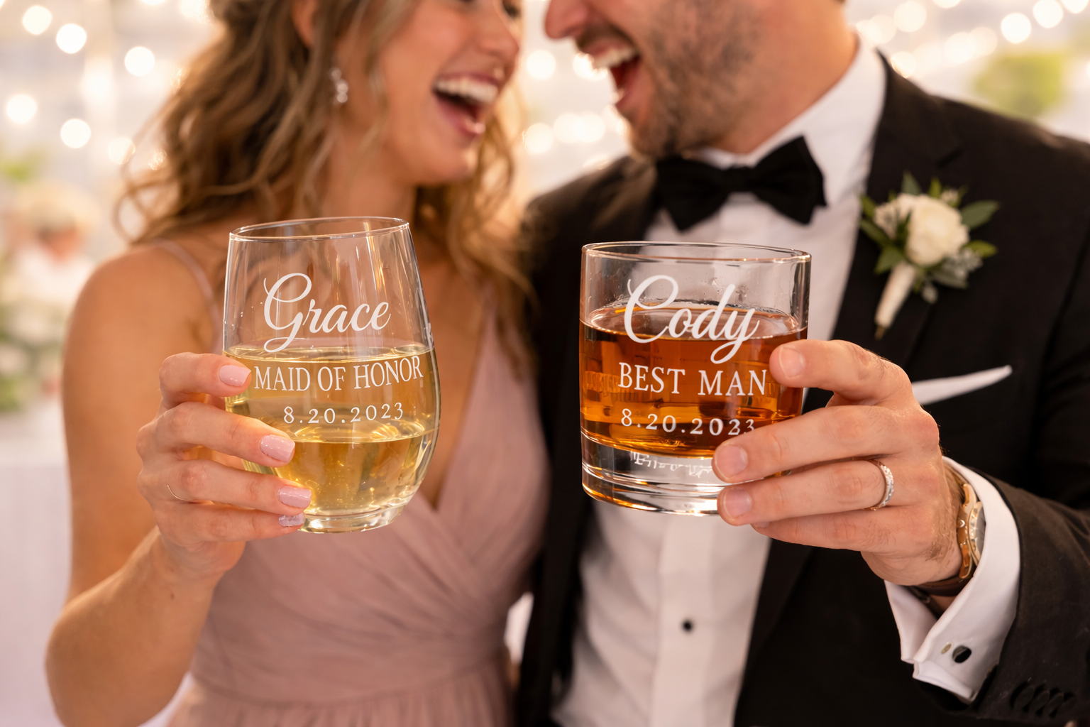 A couple celebrating their wedding, dressed in formal attire, holding personalized glasses with names and date engraved, smiling and laughing at each other.