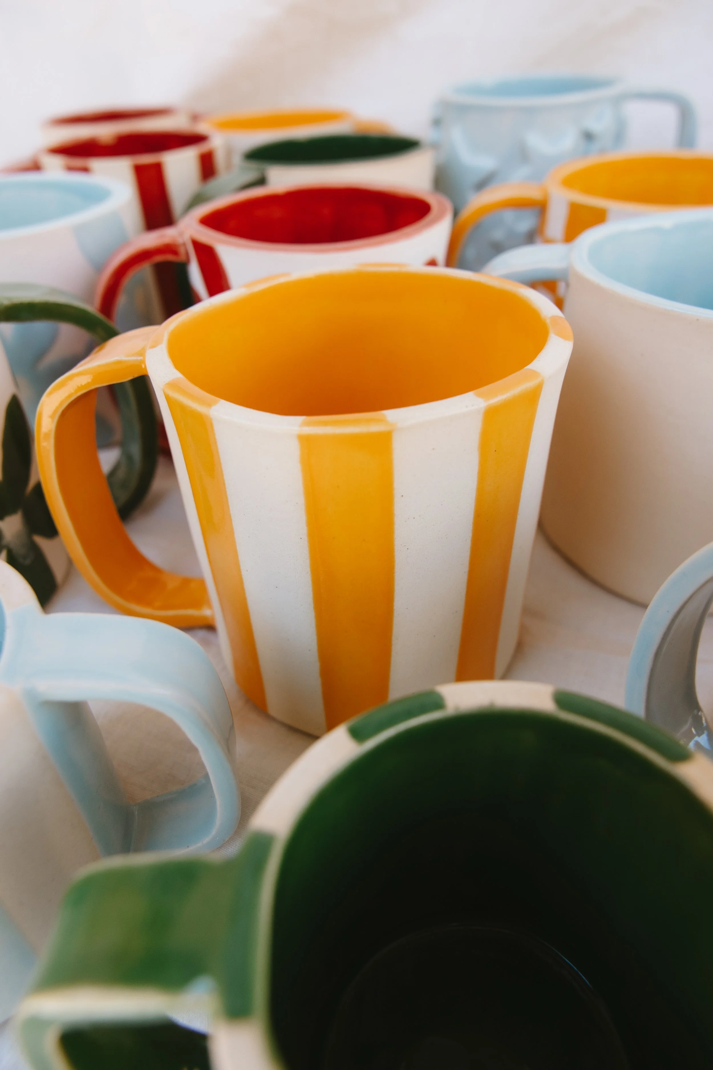 Colorful ceramic mugs with various patterns and colors, stacked and arranged on a table.