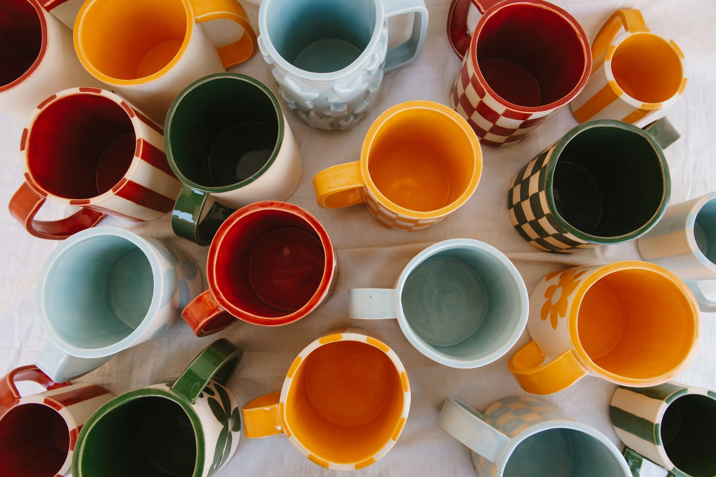 Top view of colorful ceramic mugs with various patterns and colors arranged on a white surface.