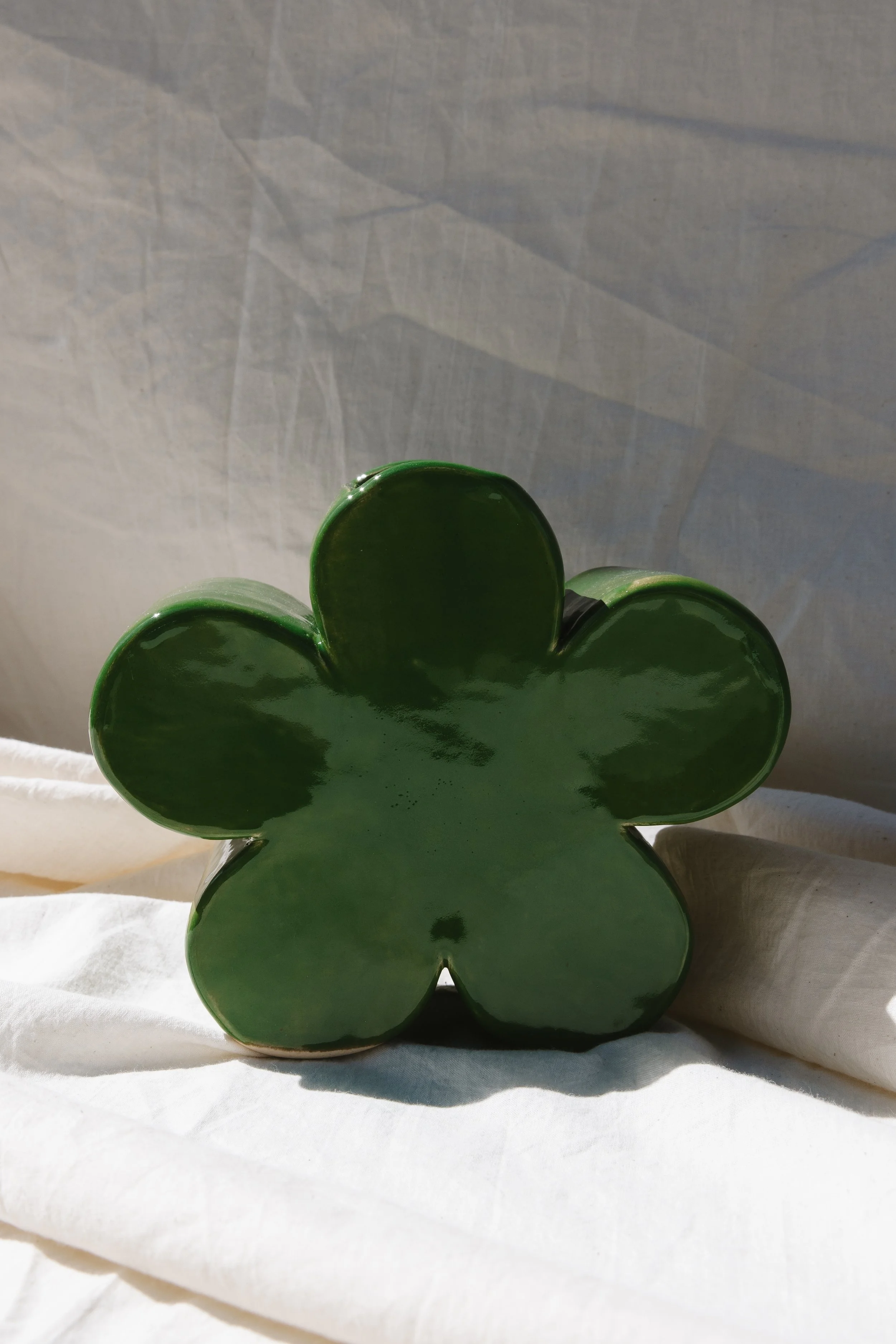 Green flower-shaped vase placed on white fabric with a neutral background.