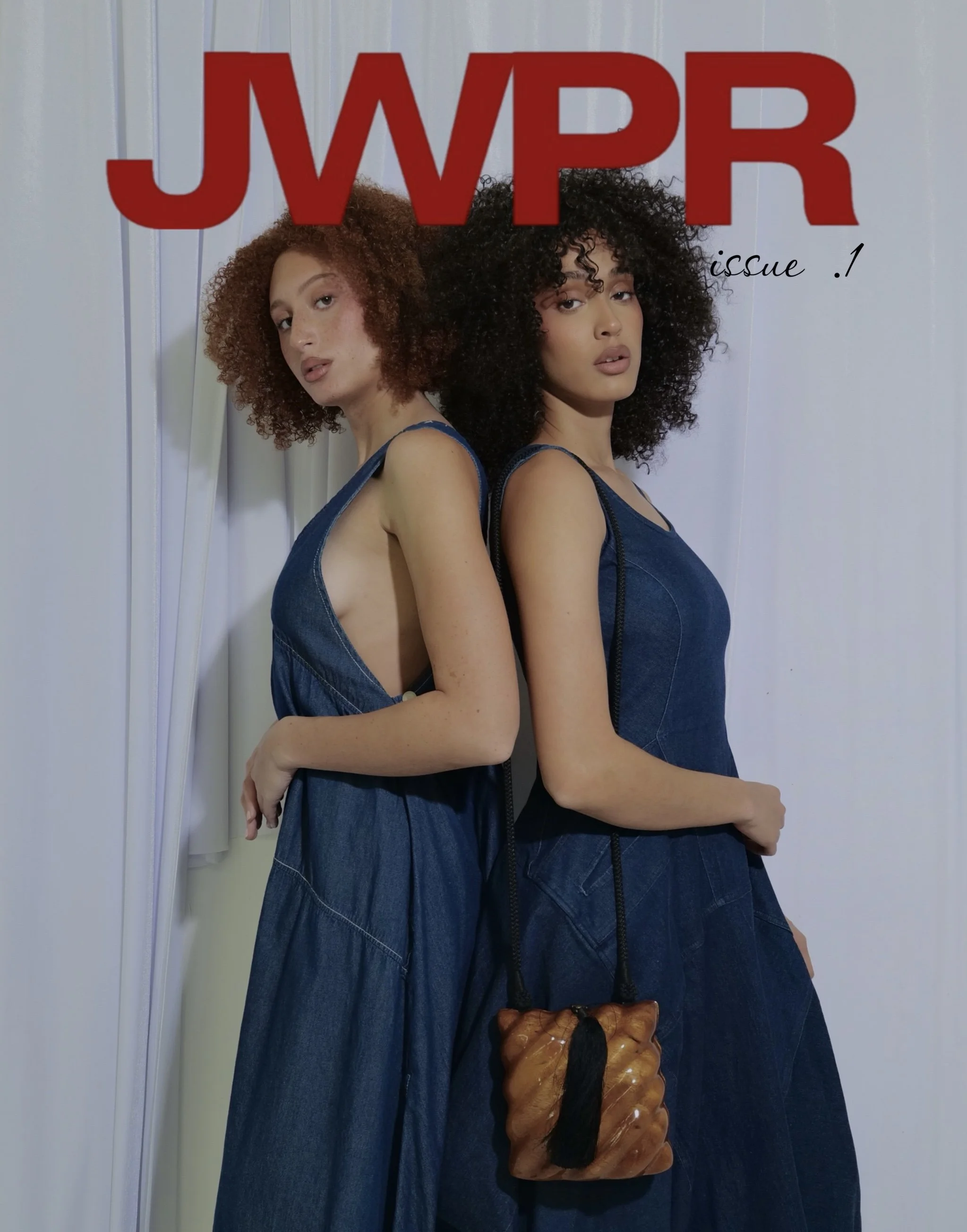 Two women with curly hair and denim dresses standing back to back, holding bags, on a magazine cover titled 'JWPR Issue 1'. 