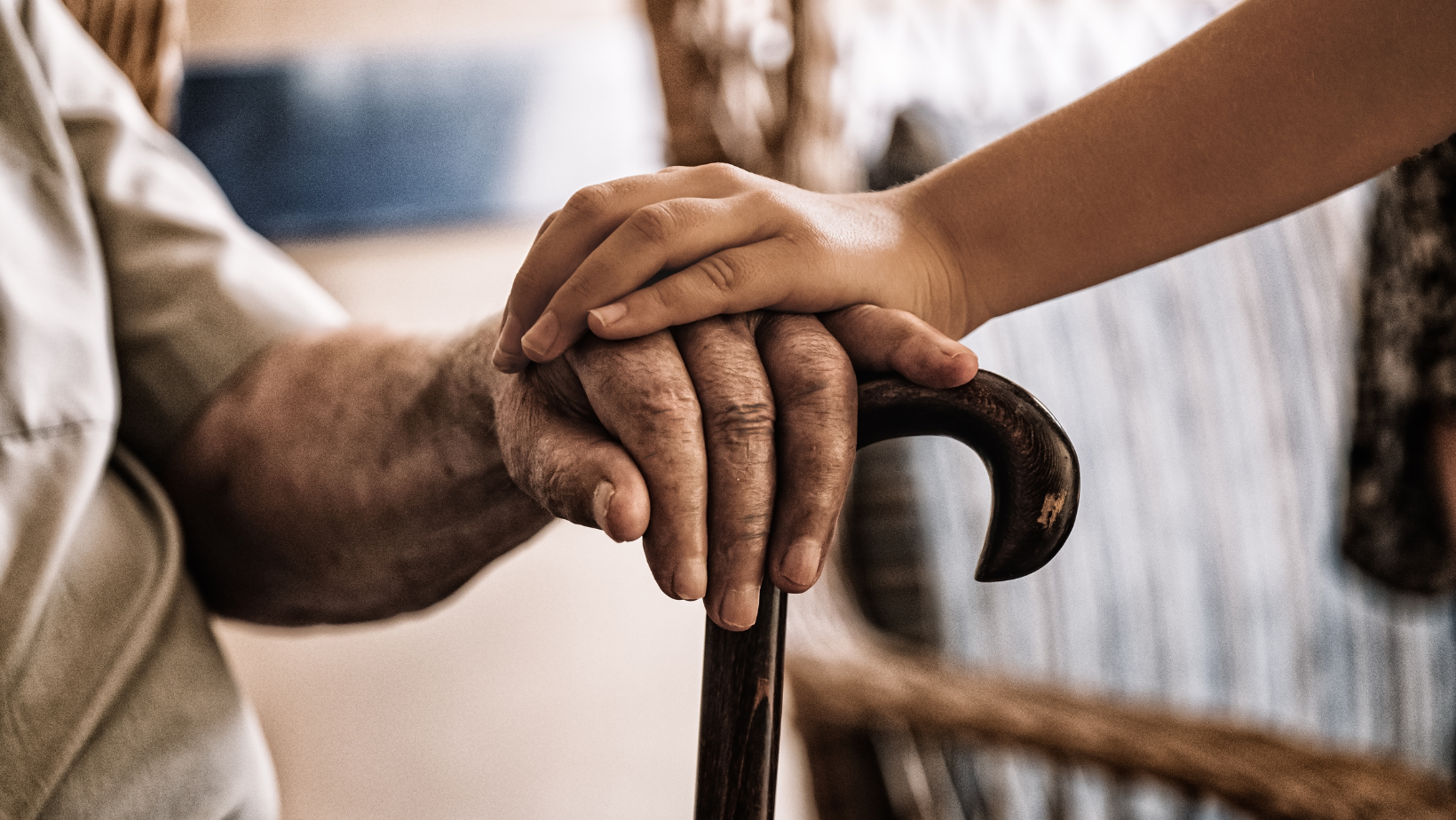 A young person's hand resting on an elderly person's hand, both holding a cane.