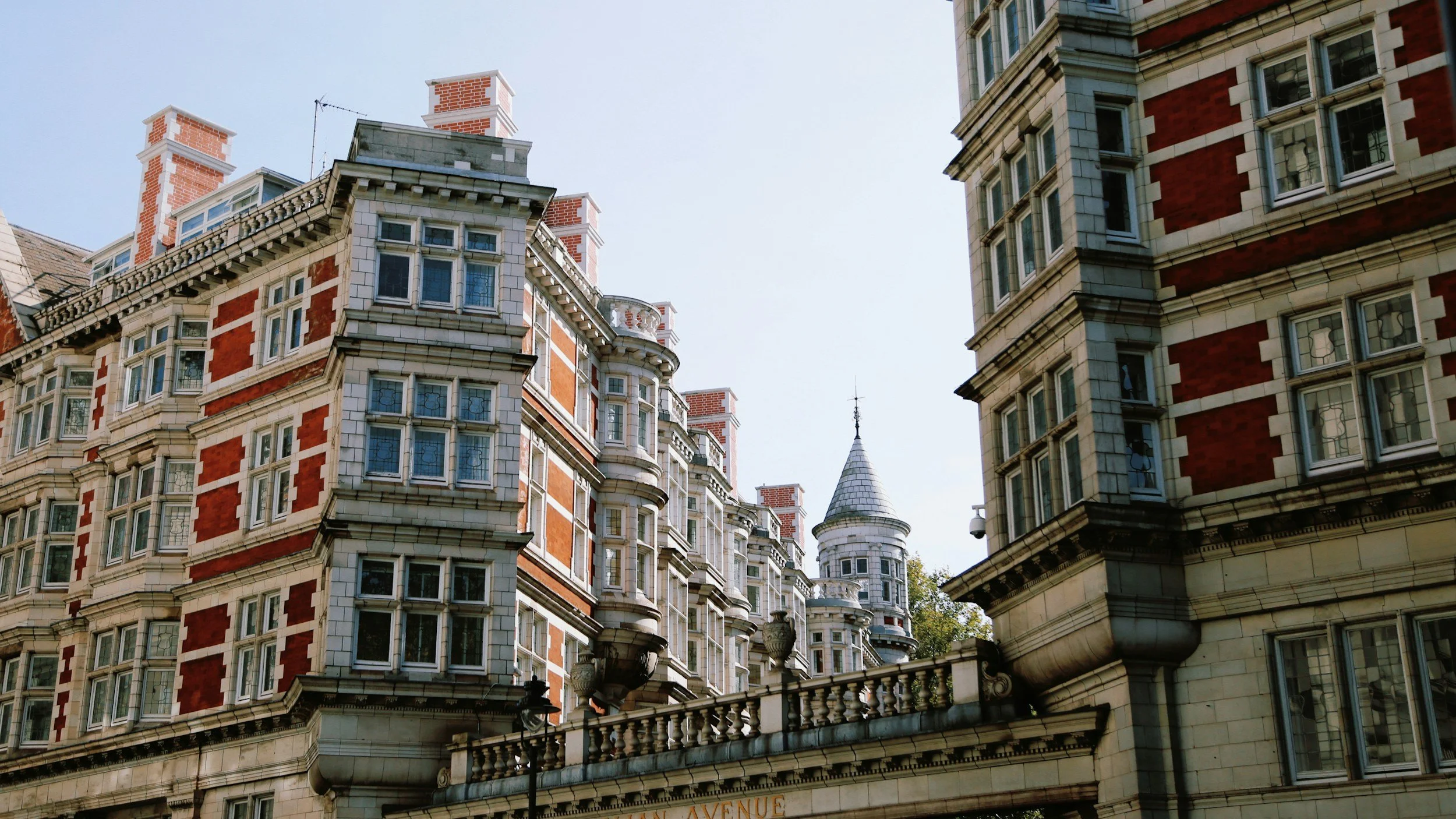 Multiple historic European-style buildings with ornate details, bay windows, and brick and stone facades, topped with chimneys and small towers, under a clear sky.