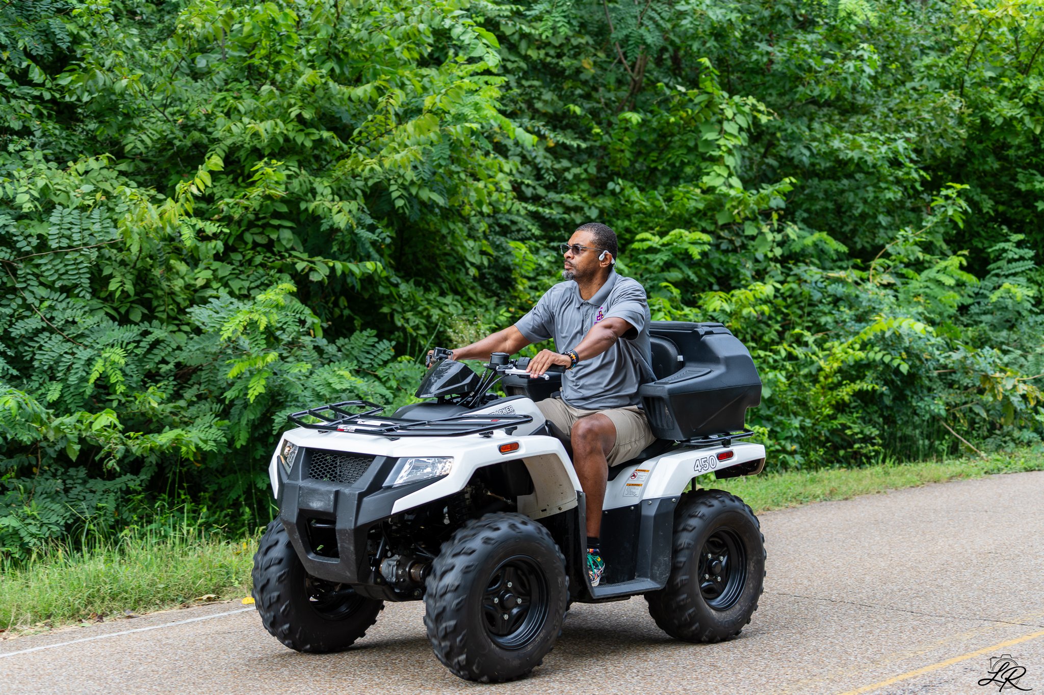 A man riding an all-terrain vehicle (ATV) on a paved path surrounded by dense green foliage.