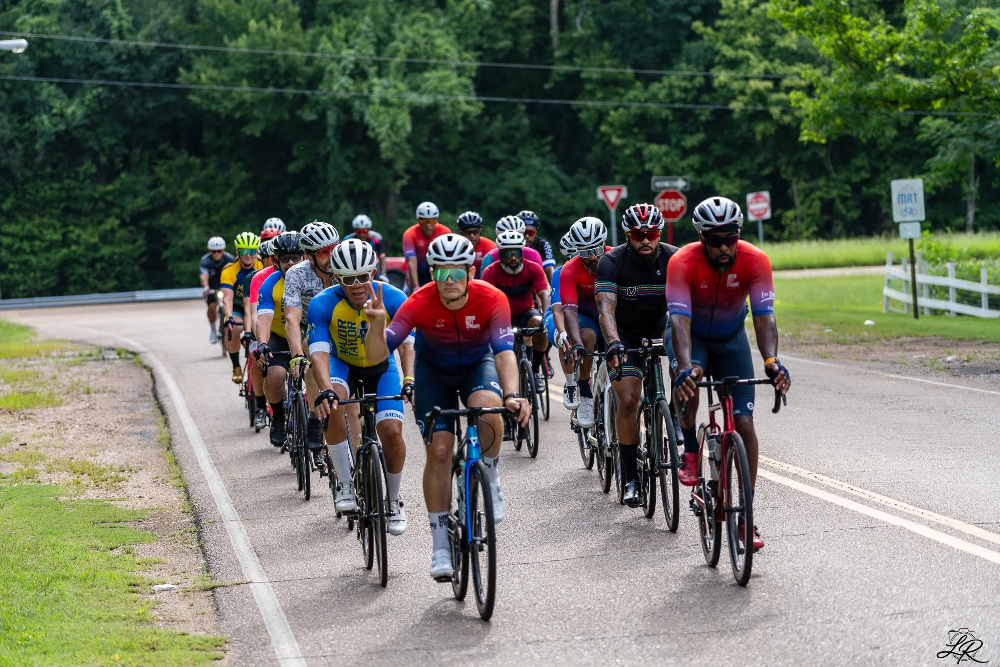 A group of cyclists riding on a road surrounded by green trees.