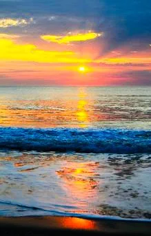 Sunset over the ocean with colorful clouds and waves.