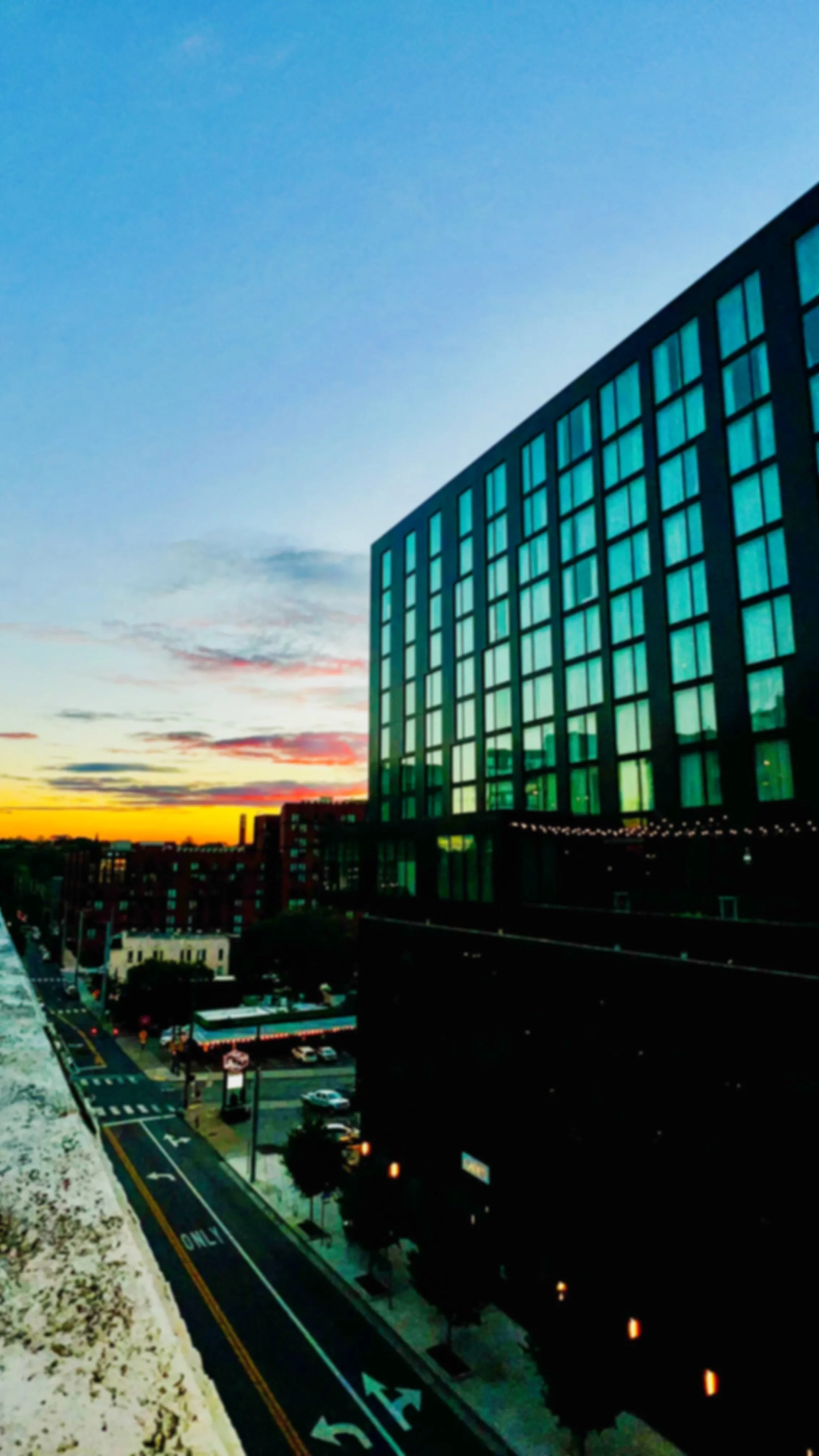 City street view during sunset with a modern building featuring reflective windows on the right.