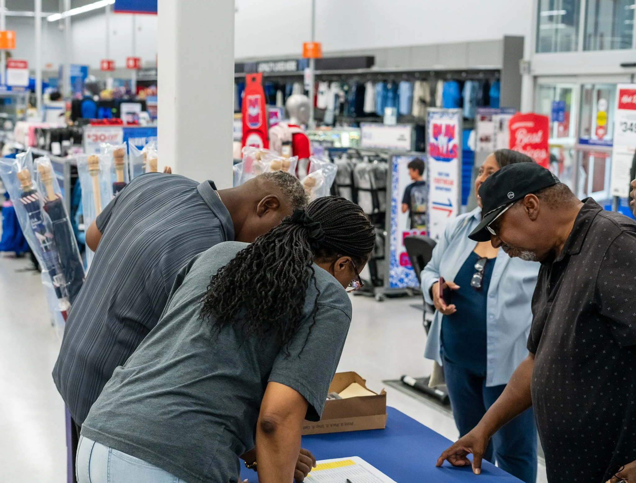 People gather around a table at a checkout counter in a retail store, engaged in a discussion or signing documents.