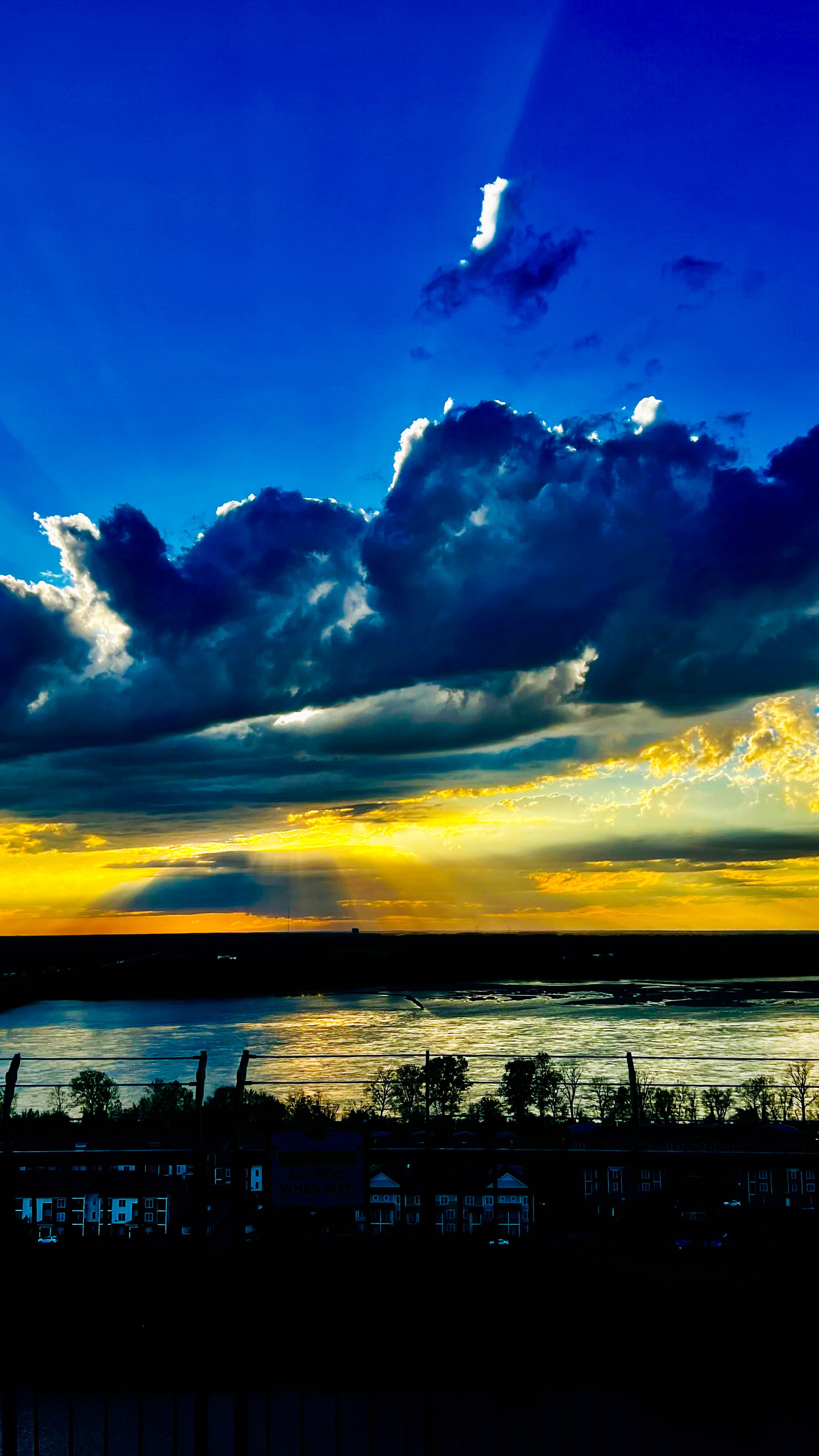 Sunset over a body of water with clouds in the sky and a fence in the foreground.