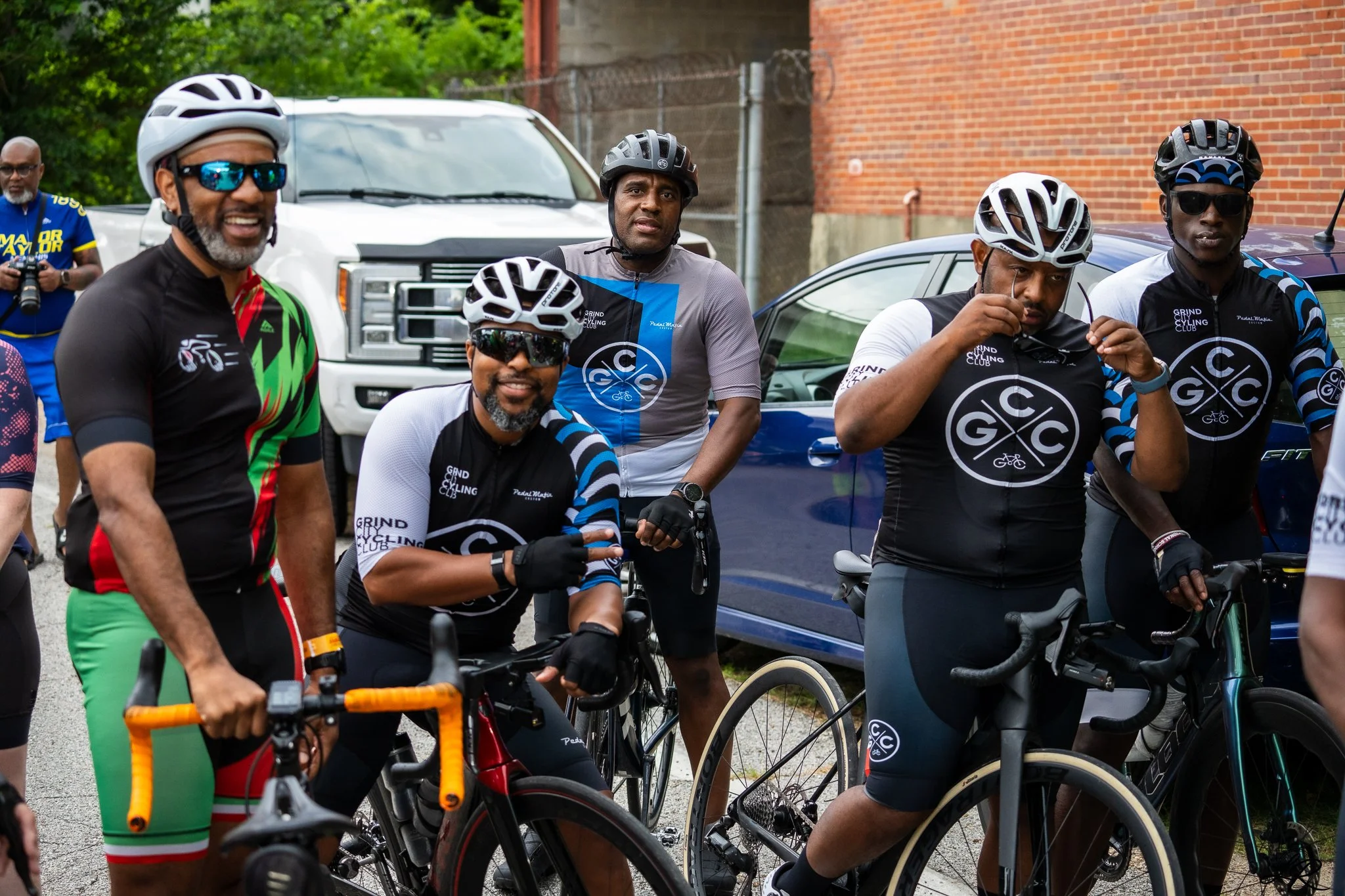 A group of men with bicycles, wearing helmets and cycling jerseys, standing on the street during a cycling event.
