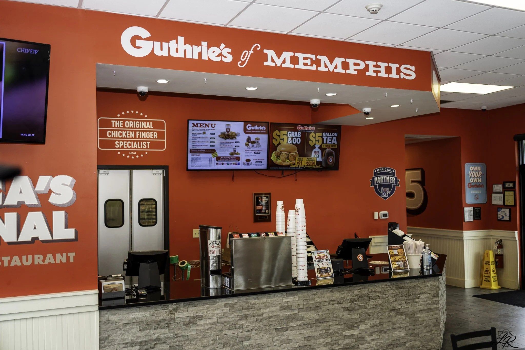 Guthrie's of Memphis fast-food counter with a red wall, menu screens, and cups on the counter.