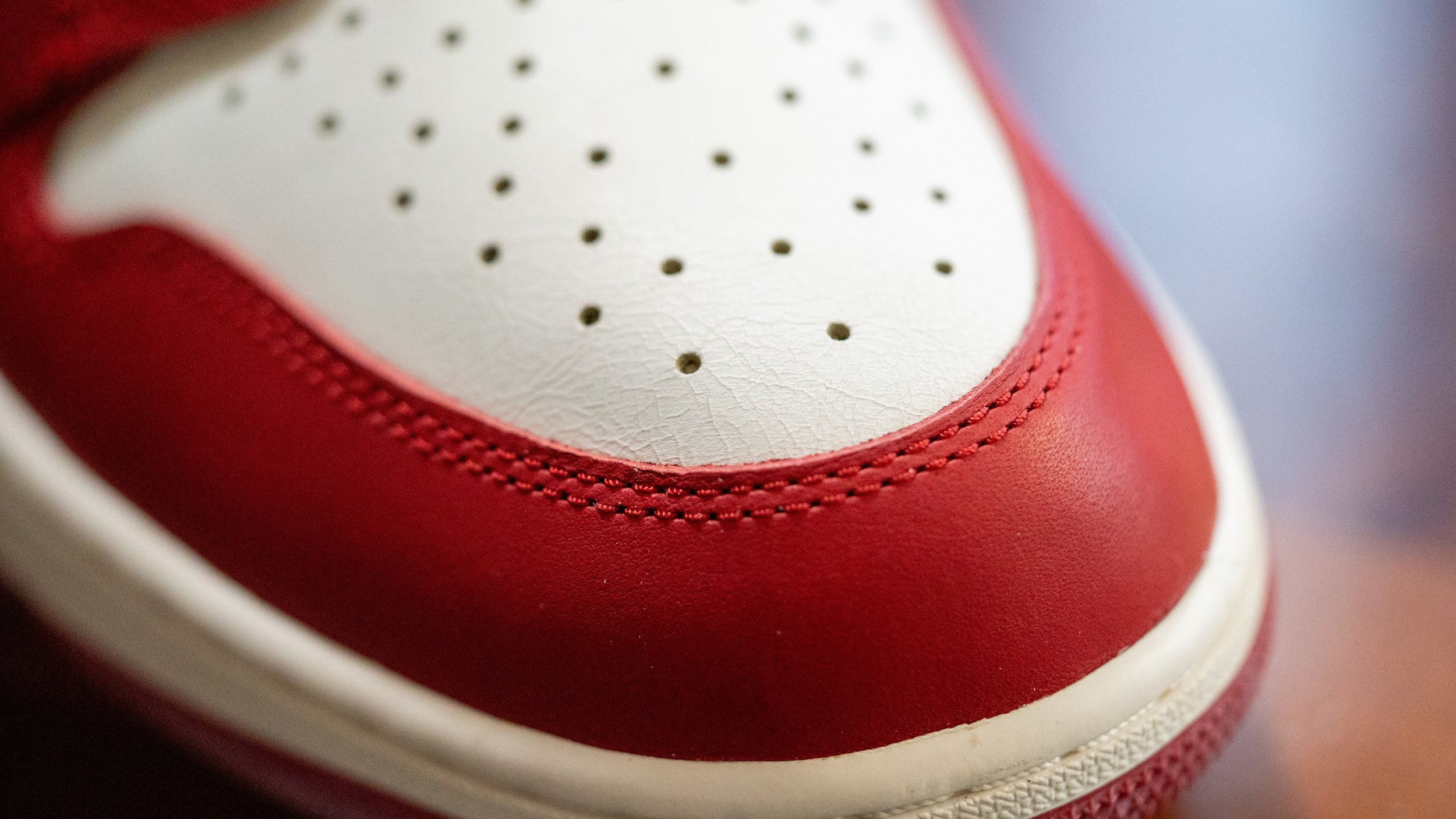 Close-up of a red and white leather sneaker showing detailed stitching and perforations on the toe box.