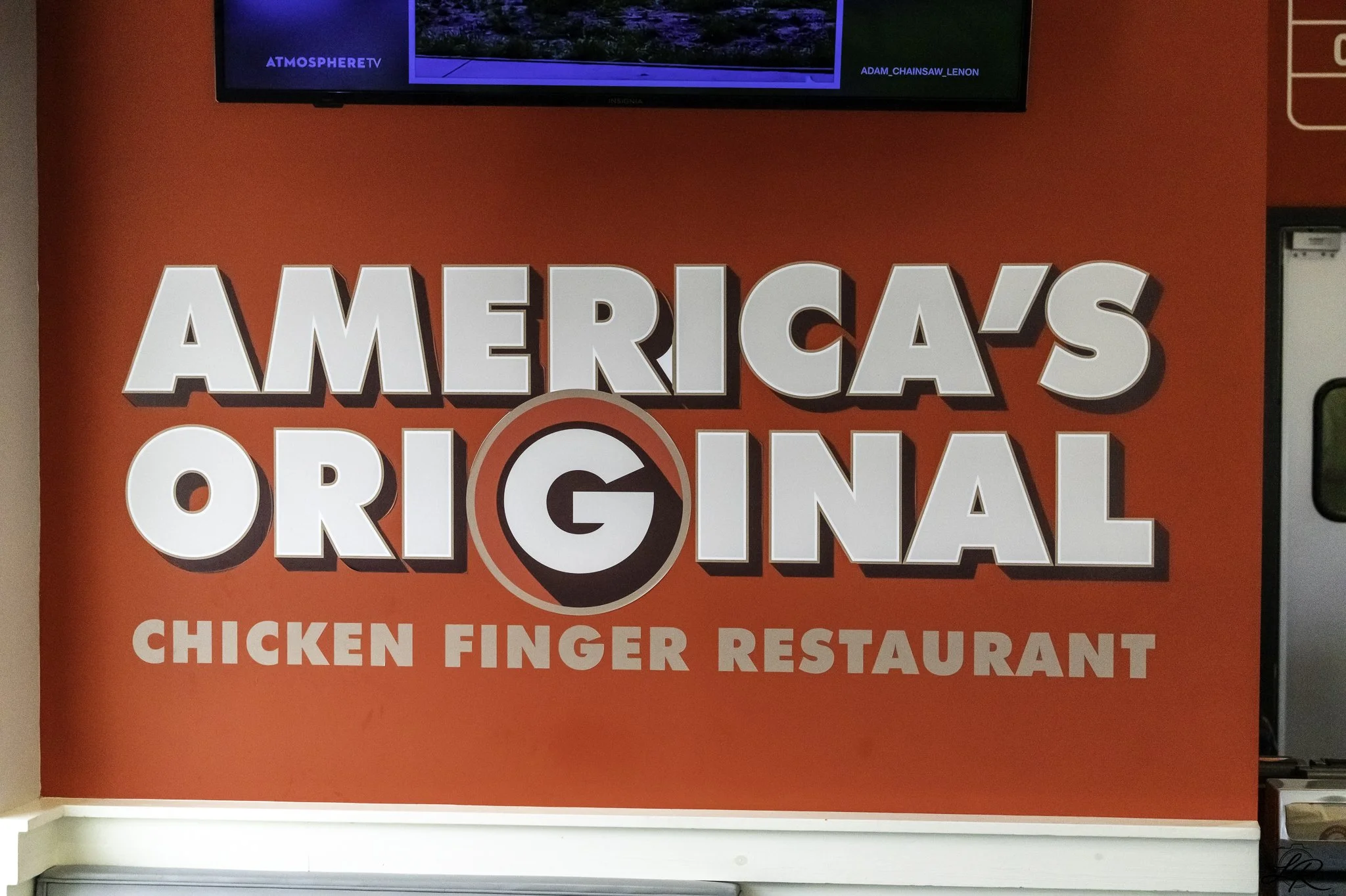Sign for America’s Original Chicken Finger Restaurant with a red background and the words "America's Original" in large white 3D letters, and "Chicken Finger Restaurant" in smaller pink letters below.