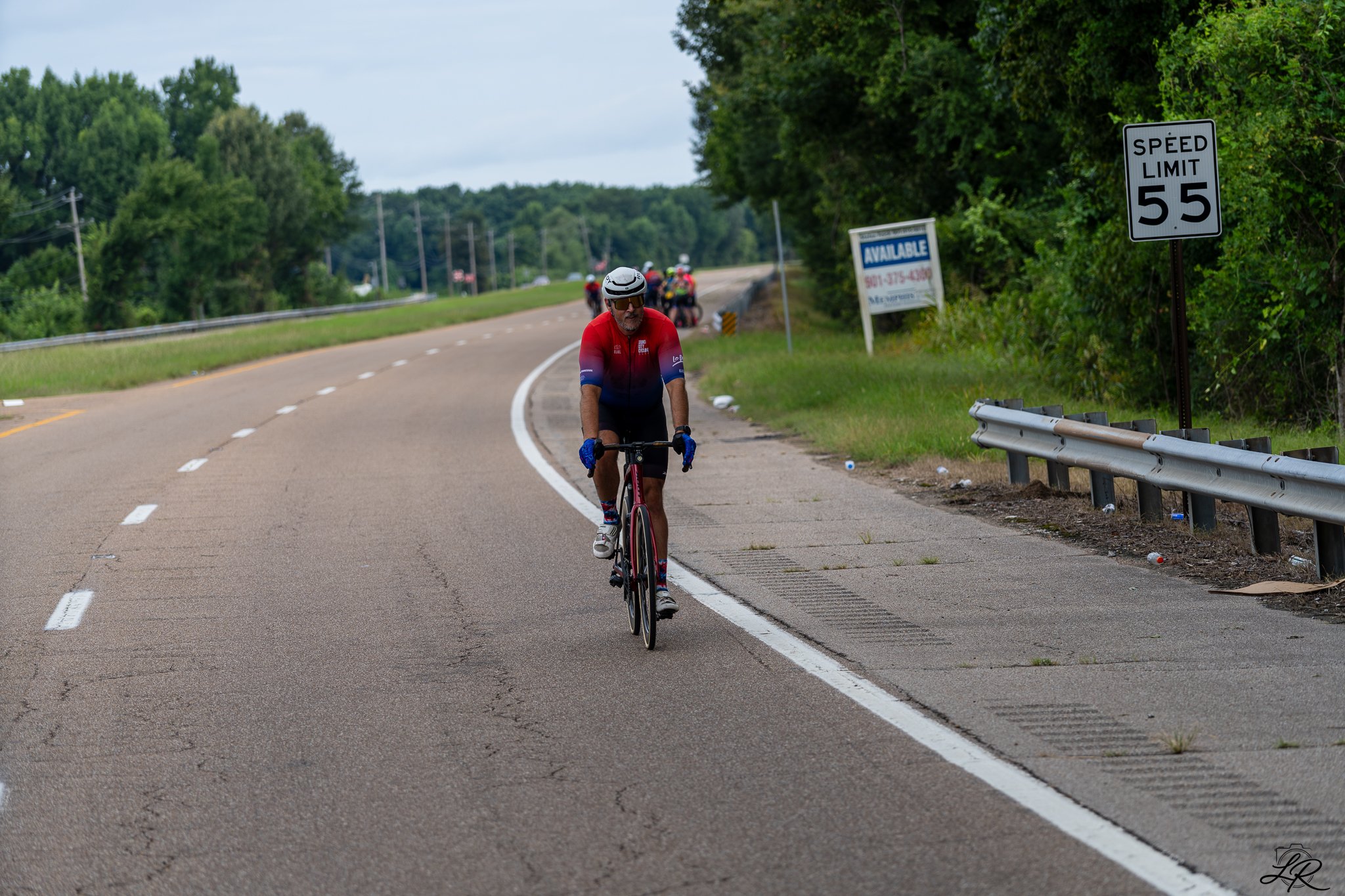 A man riding a bicycle on a rural road with a speed limit sign of 55 mph.
