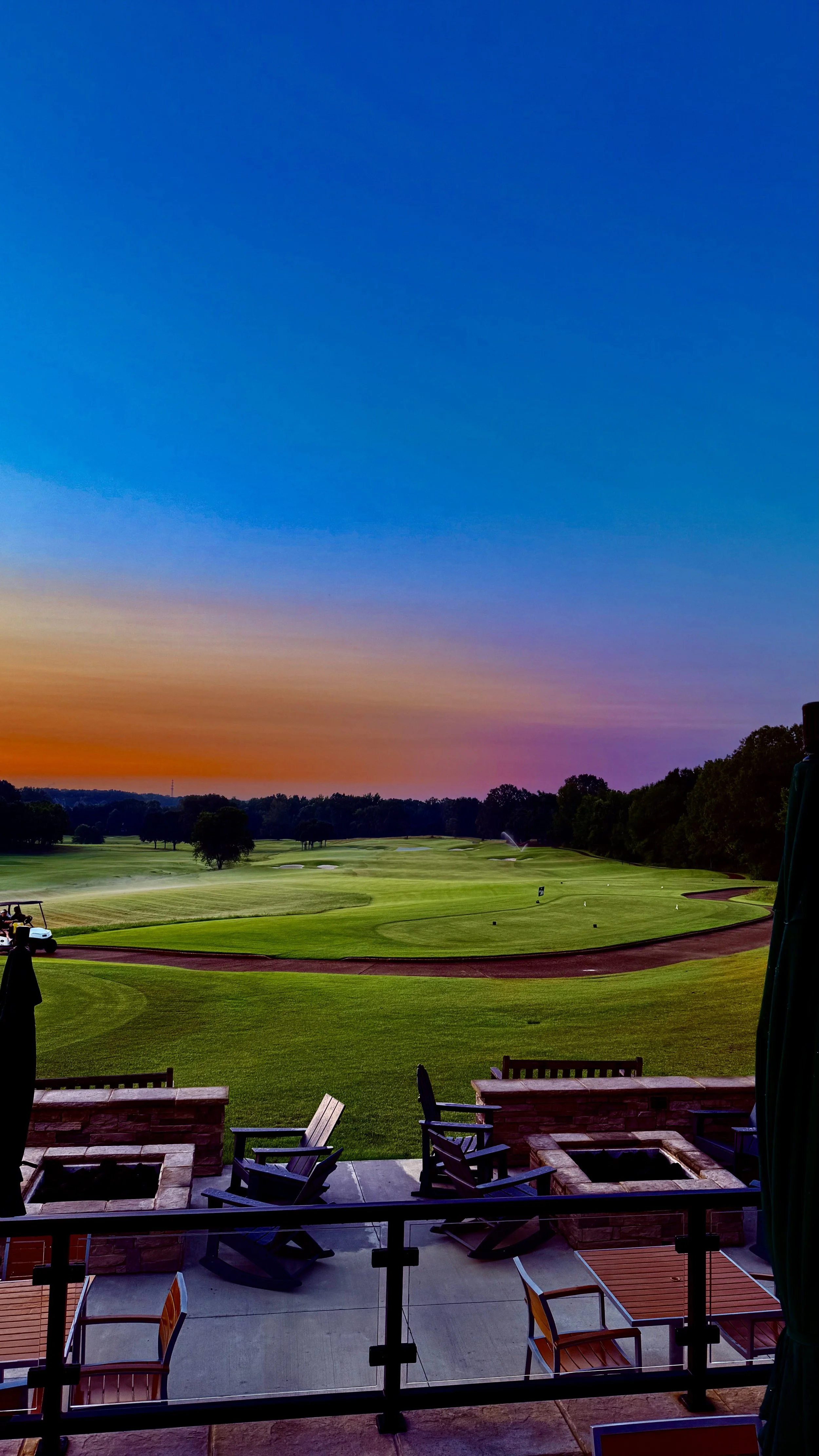 View of a golf course at sunset, seen from a patio with chairs and fire pits.