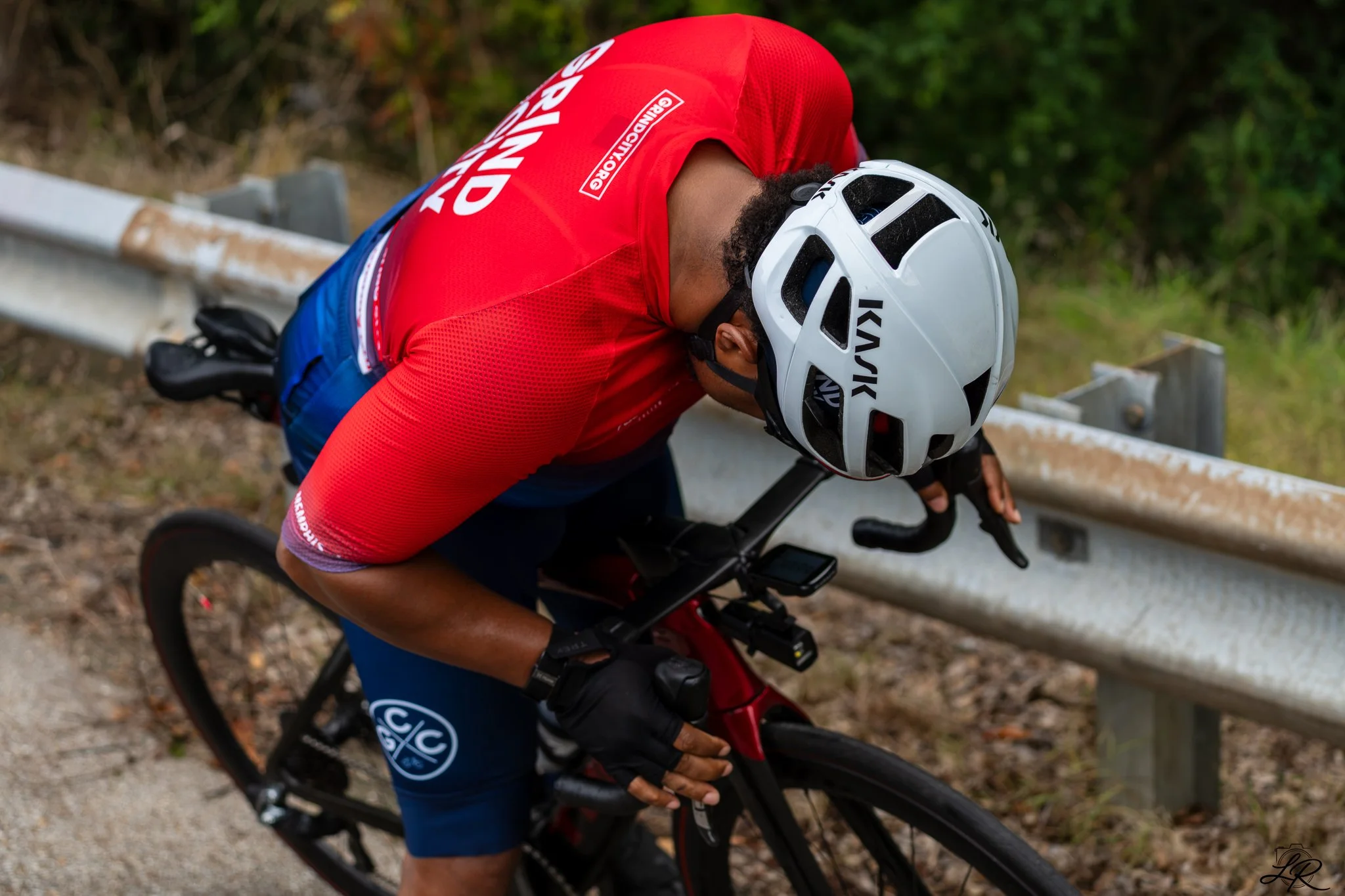 A person wearing a white helmet and red shirt riding a black bicycle on a trail near a metal guardrail.