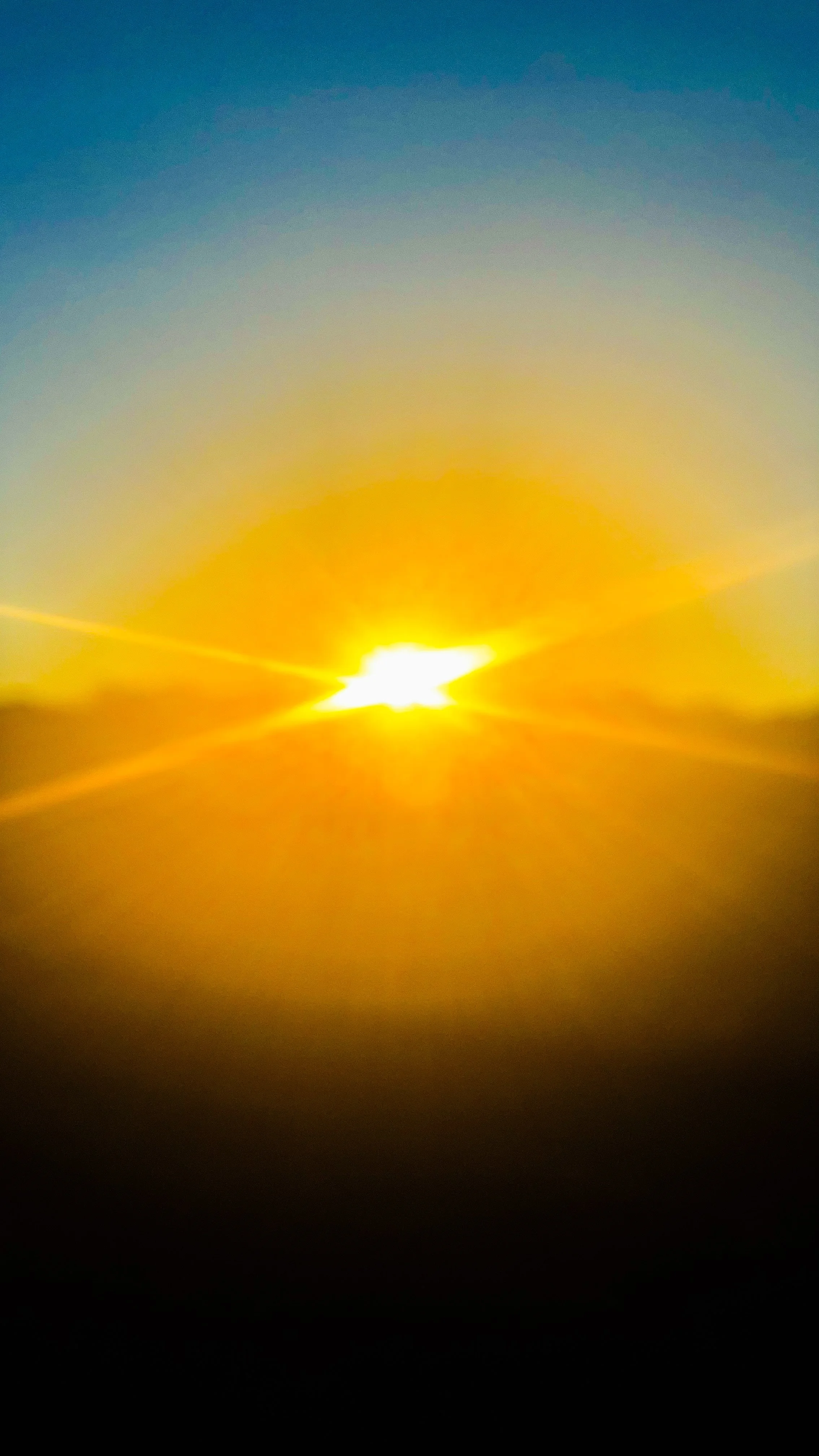 Sunset with the sun partially below the horizon, casting an orange glow in the sky with a gradient of blue and yellow hues.