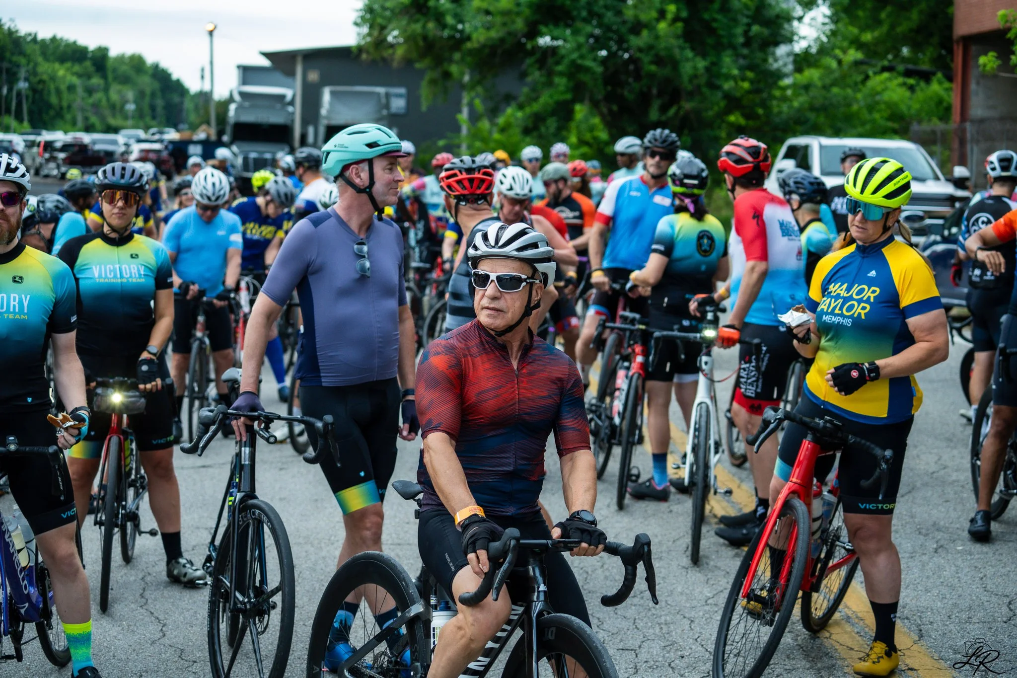 A large group of cyclists gathered outdoors, many wearing helmets and colorful cycling gear.