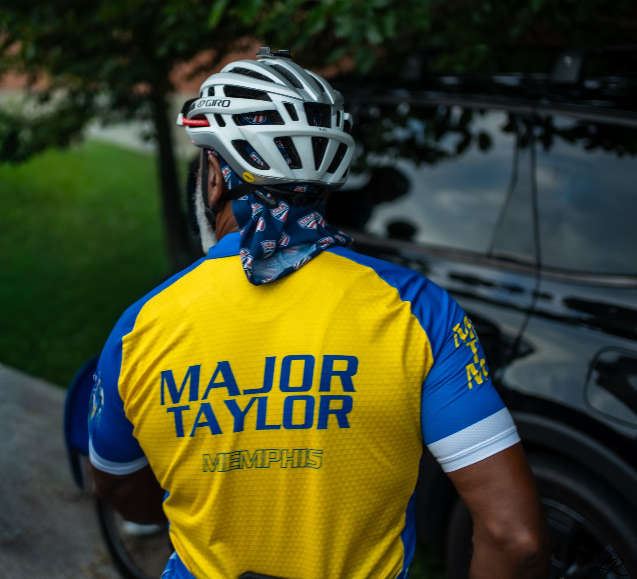 Close-up of a cyclist wearing a white helmet, a blue and yellow jersey with 