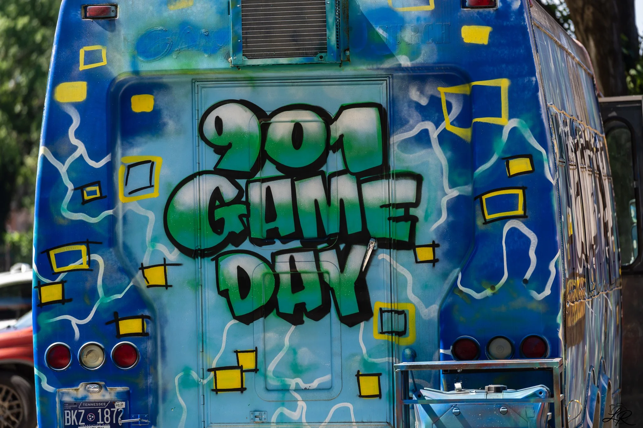Back of a bus painted with colorful graffiti in shades of blue, green, and yellow, featuring abstract shapes and a large tag reading 'You Gave' in black outlined letters.