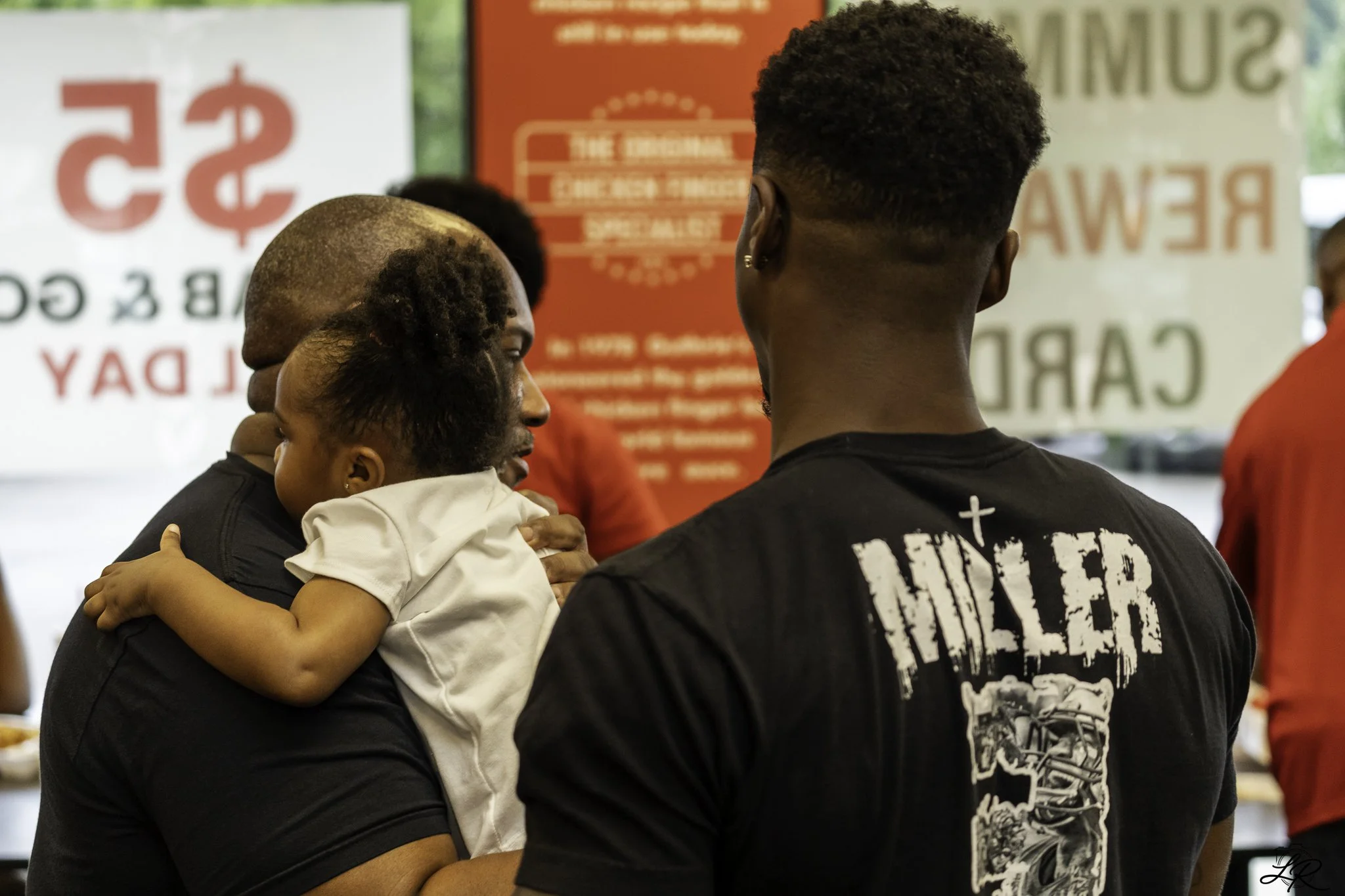 A group of people, including a man and a child, gathered in a public space with signs in the background related to a blood drive and blood donation.