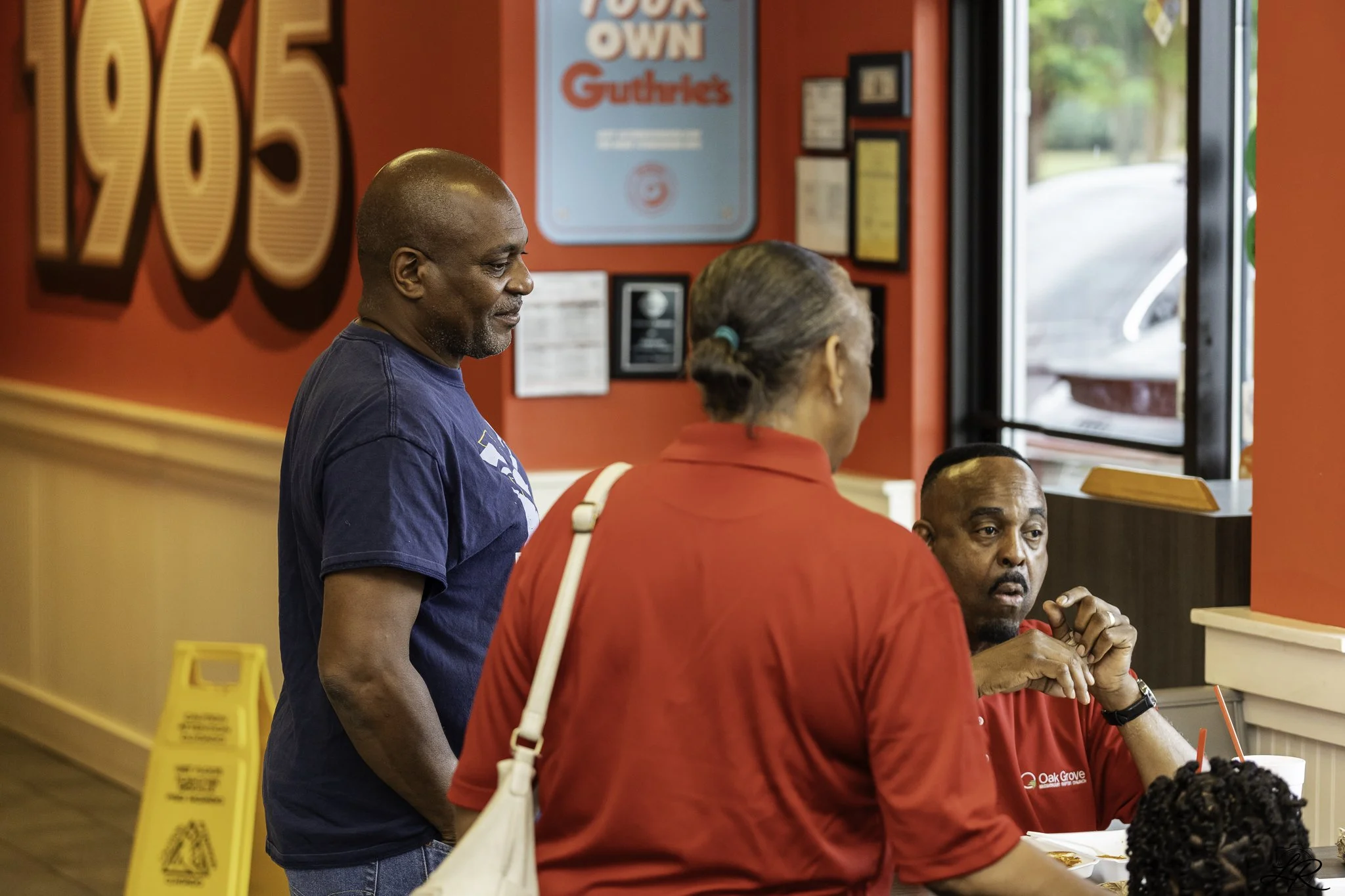 People standing in line at a fast food restaurant counter, with a red and yellow interior, and a sign that says "Build Your Own.
