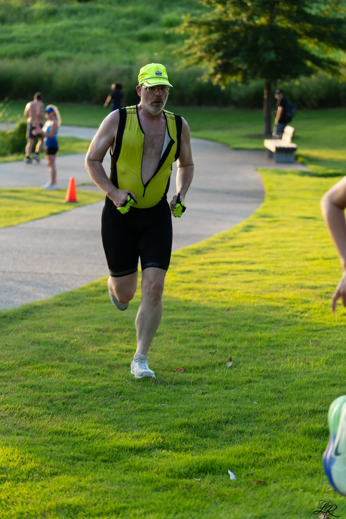 An older man in a yellow fitness outfit running outdoors in a park during daytime.