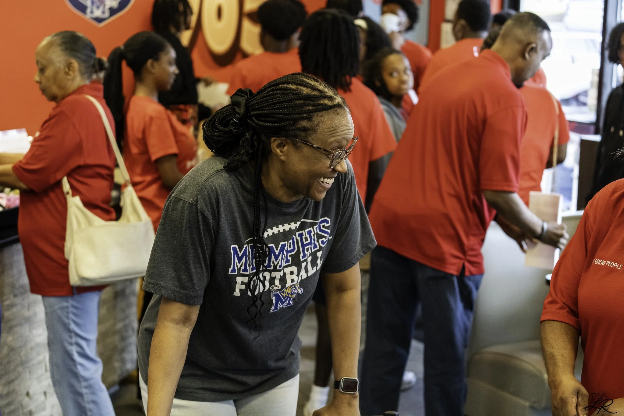 A group of people, mostly women and young girls, standing in line inside a store, some wearing red shirts.