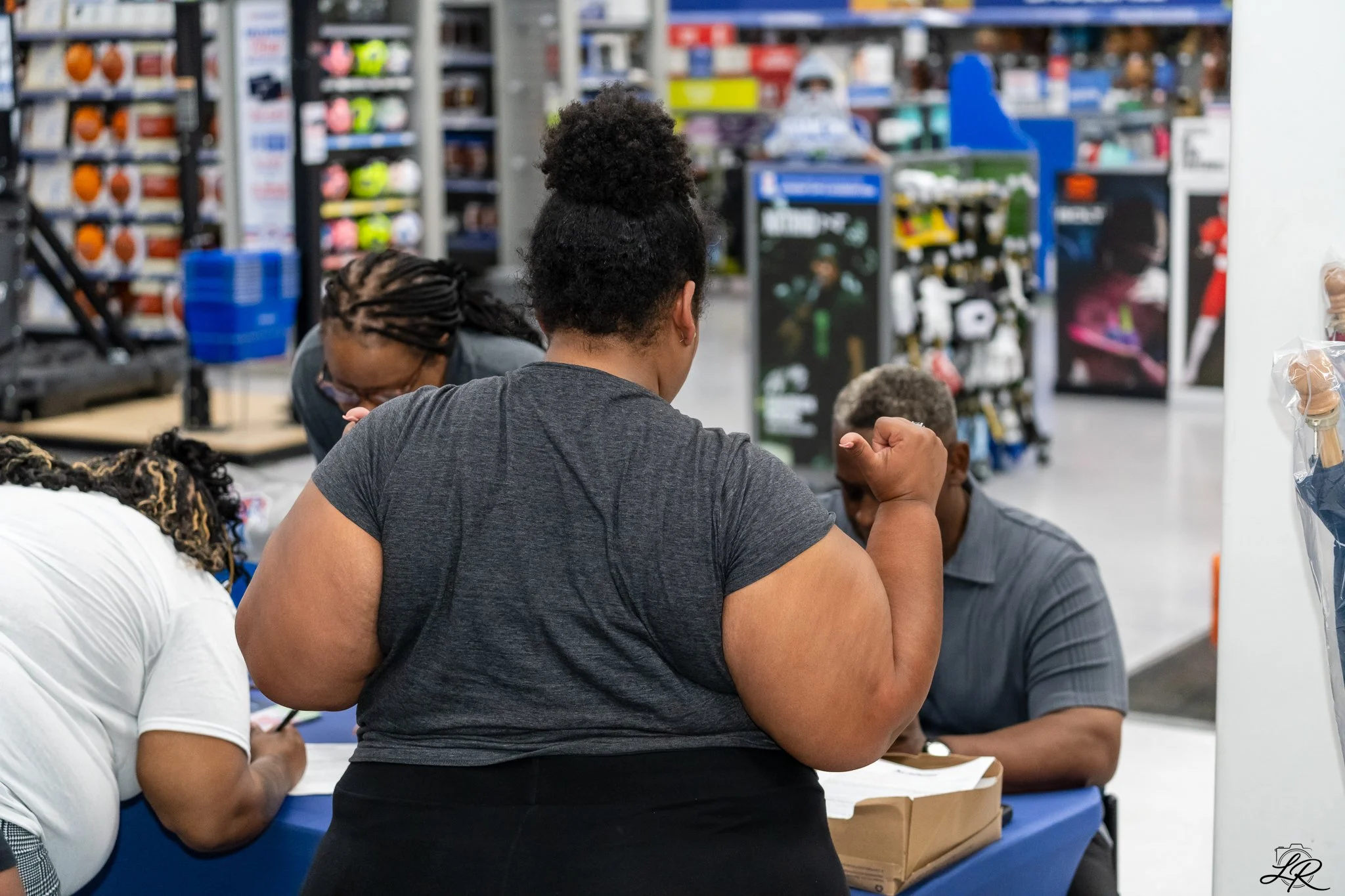 People sitting at a table in a store or warehouse, with shelves of products in the background, engaging in a discussion or activity.